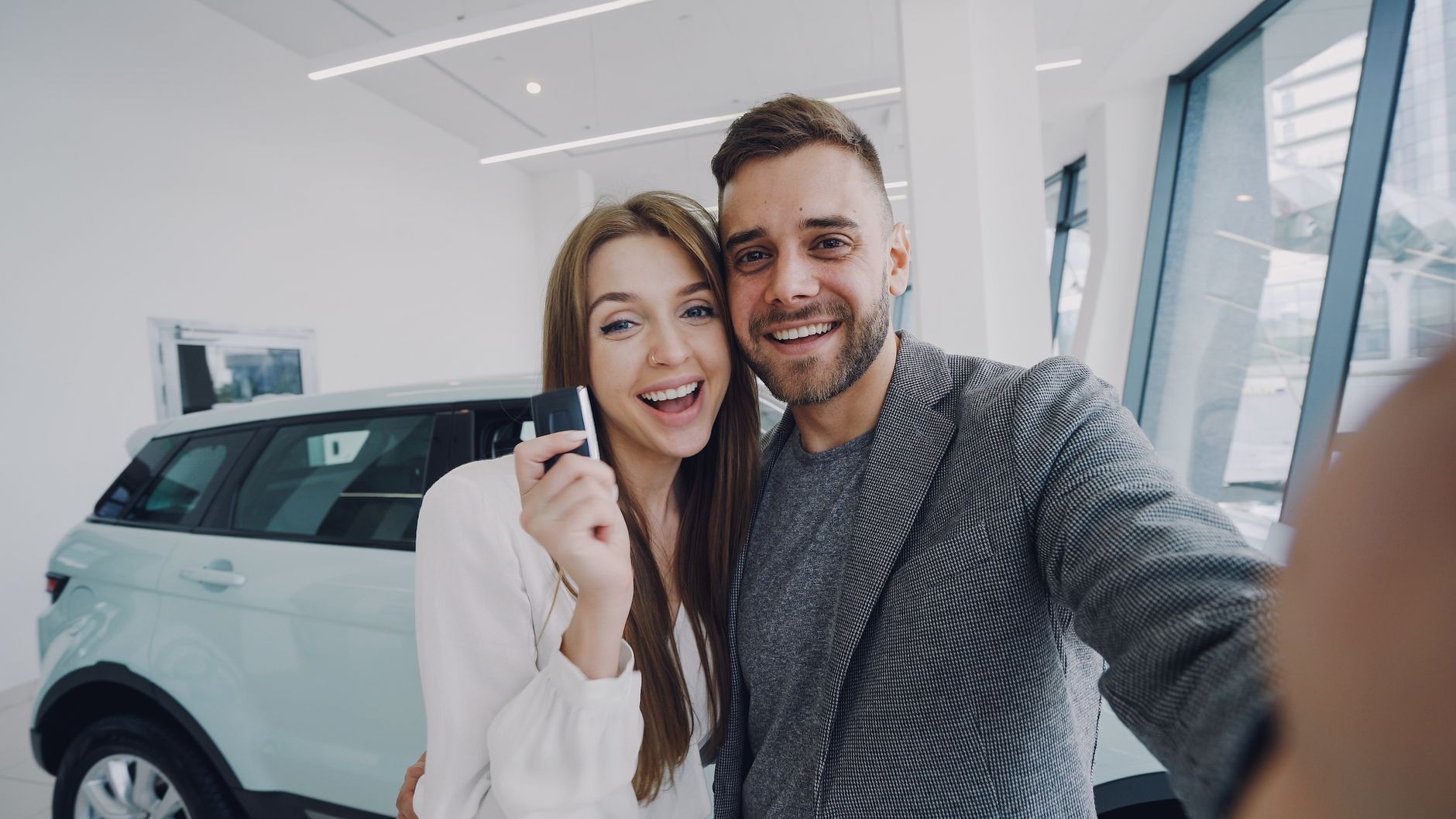 A joyful couple taking a selfie after purchasing a new car, indoors.