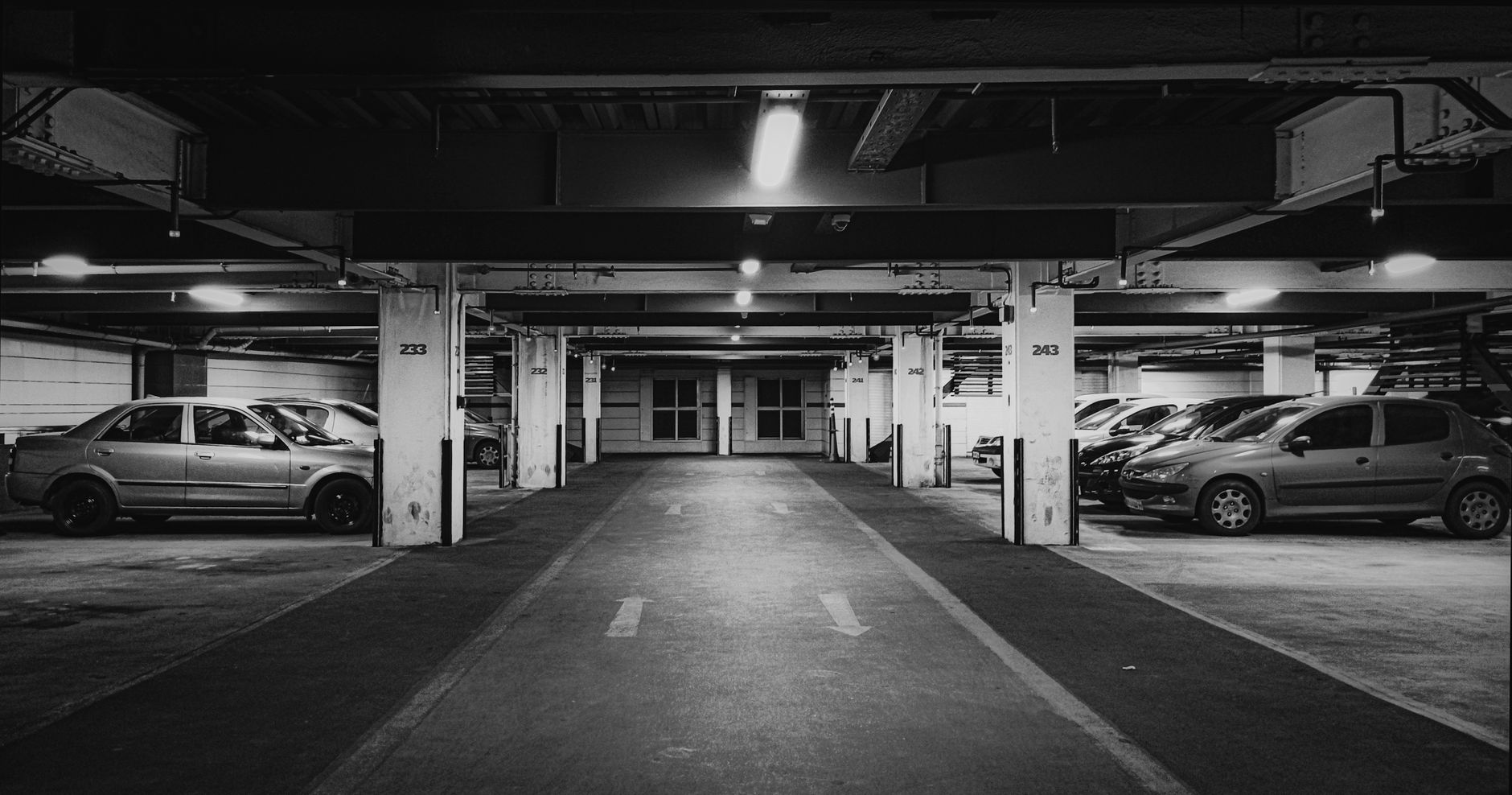 Black and white photo of an underground parking lot with cars and strong contrast lighting.