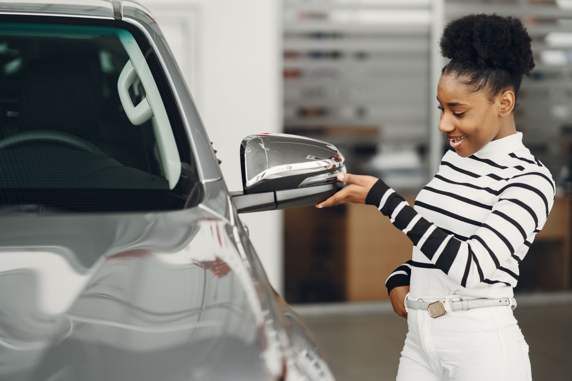 A cheerful woman admires a silver vehicle in a modern showroom, symbolizing automotive enthusiasm.