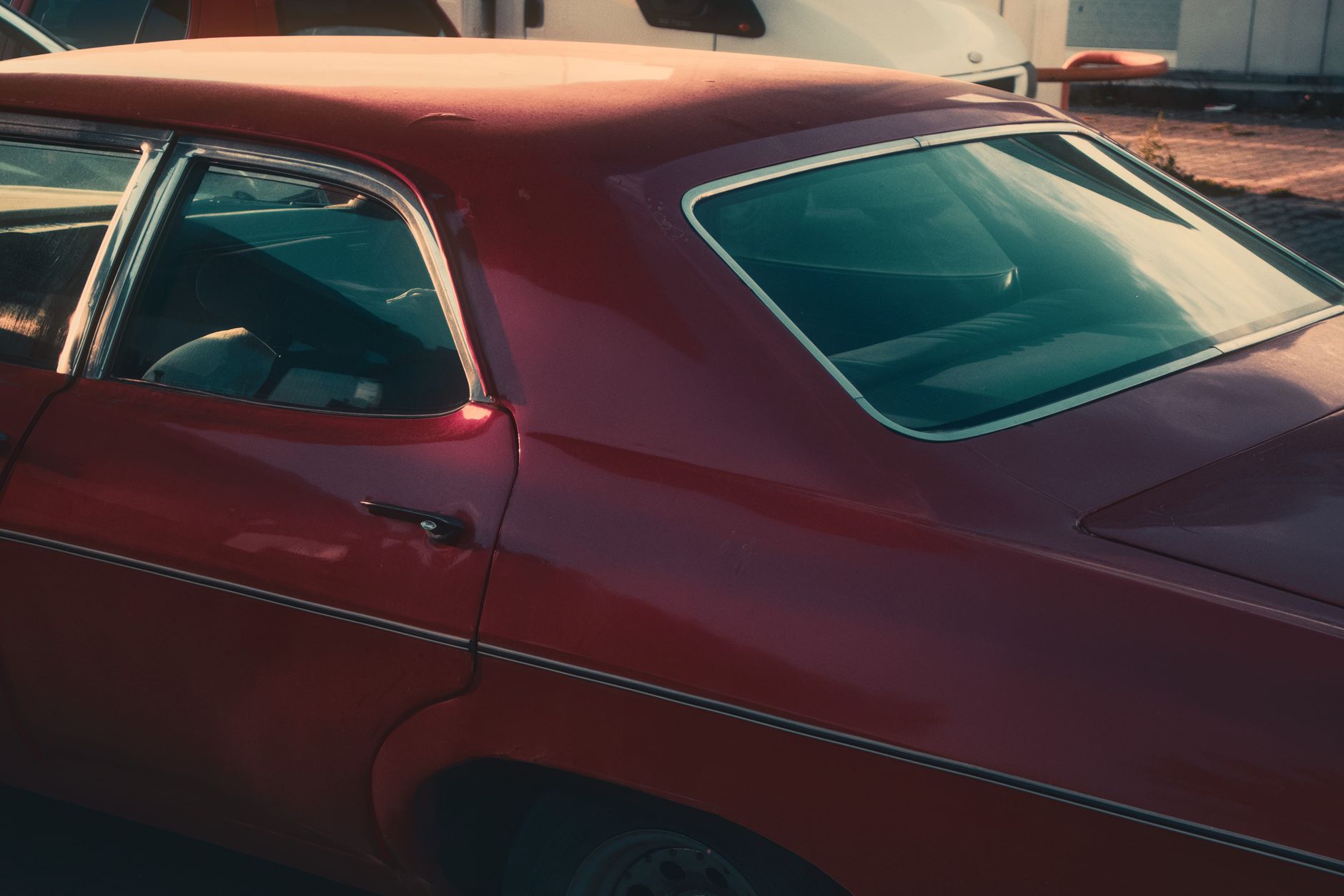 Side view of a parked red vintage car, showcasing classic design in warm lighting.