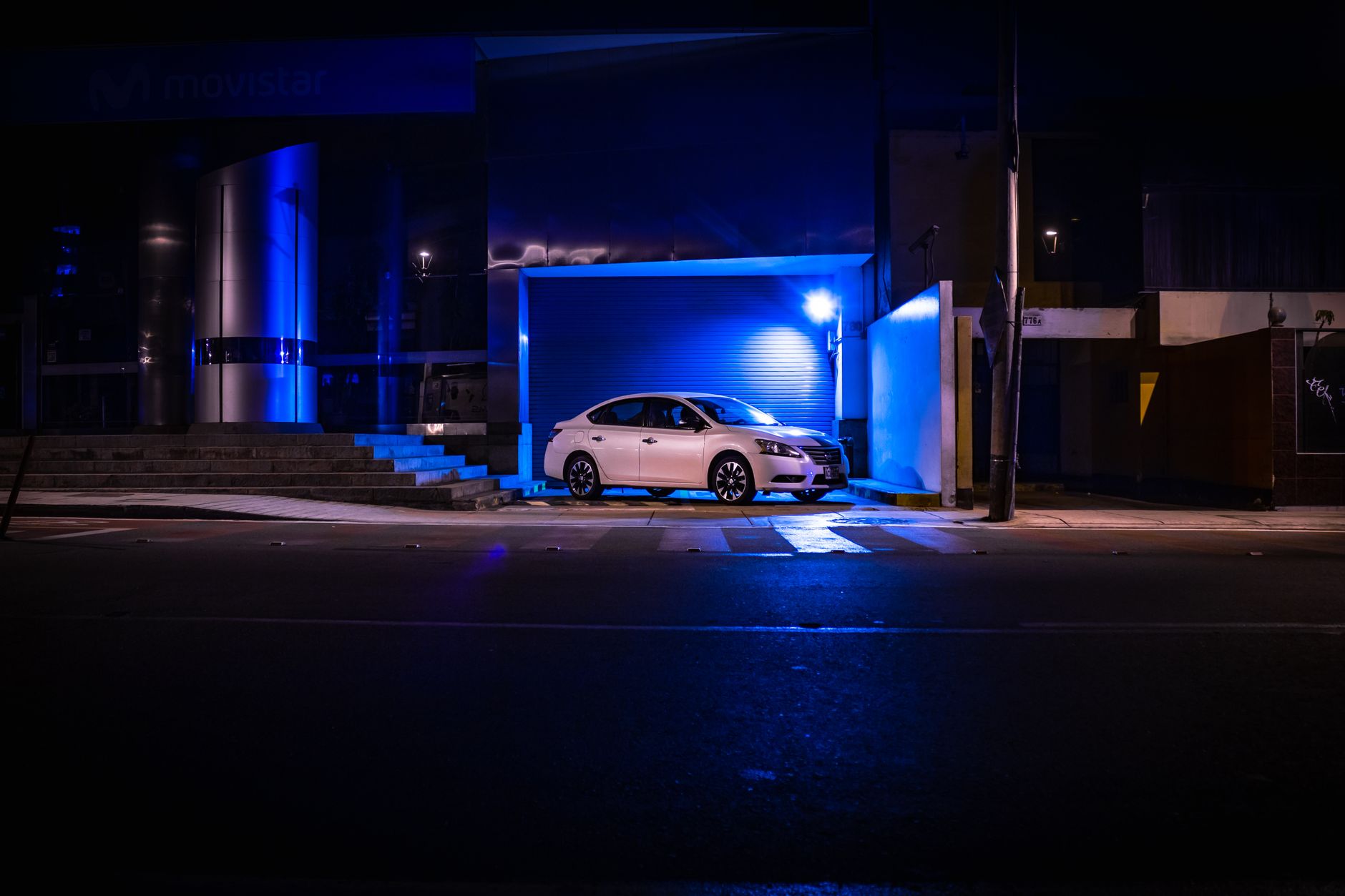 Stylish white car parked in an illuminated suburban area at night with urban blue lighting.