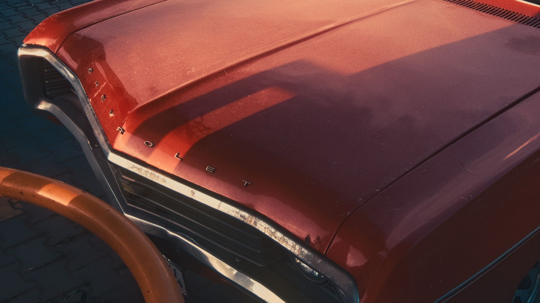 A classic red car hood with a retro vibe captured at sunset, casting warm reflections.