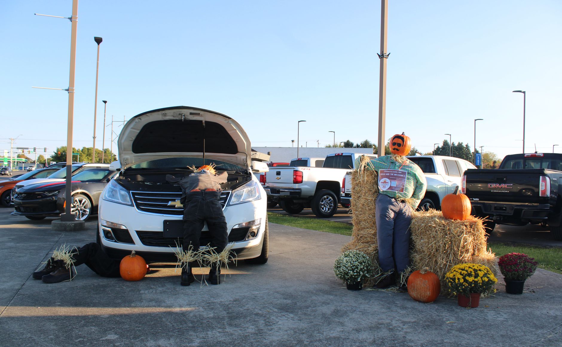 Halloween scarecrow display with cars and pumpkins in an outdoor setting.