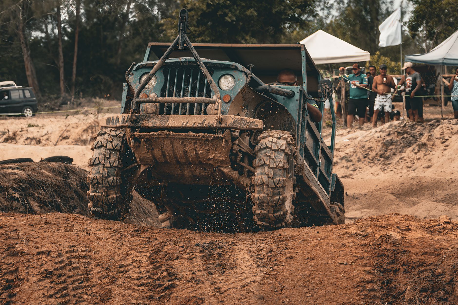 A rugged off-road vehicle powers through a muddy track as onlookers watch the thrilling outdoor event.
