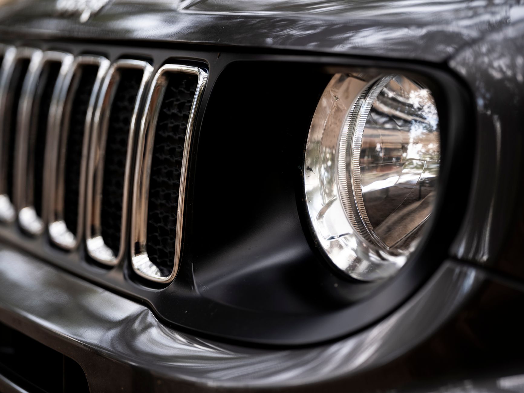 Detailed view of a black Jeep SUV headlight and grille, emphasizing its rugged design.