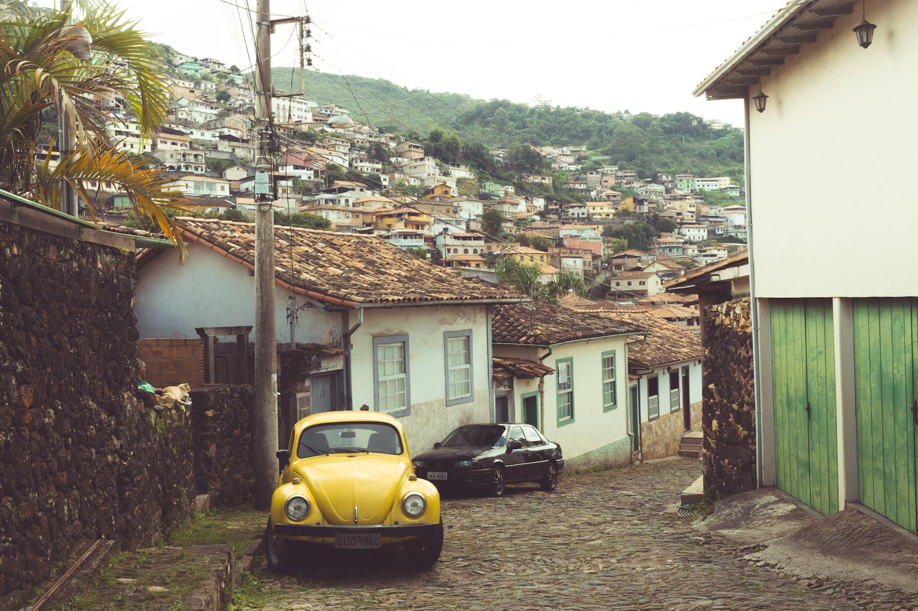 Charming cobblestone street in Ouro Preto, Brazil featuring colonial architecture and a classic yellow car.