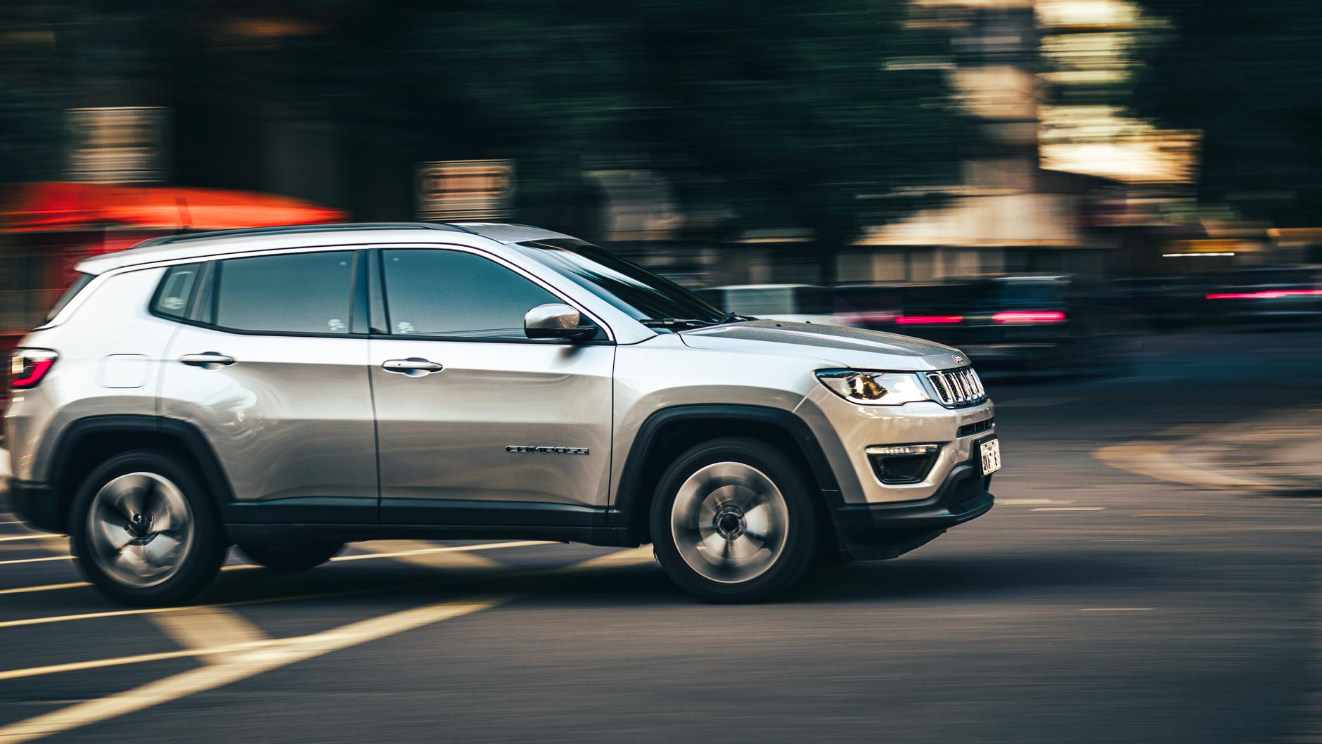Dynamic side view of a silver SUV speeding downtown, capturing urban motion.