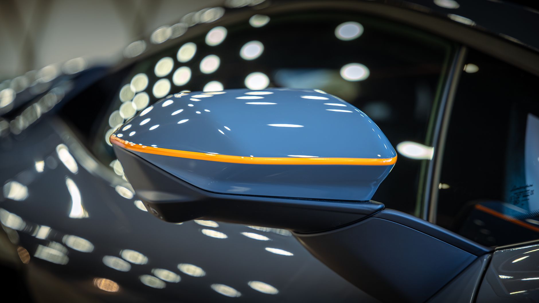 Detailed close-up of a stylish car side mirror reflecting ceiling lights in a showroom setting.