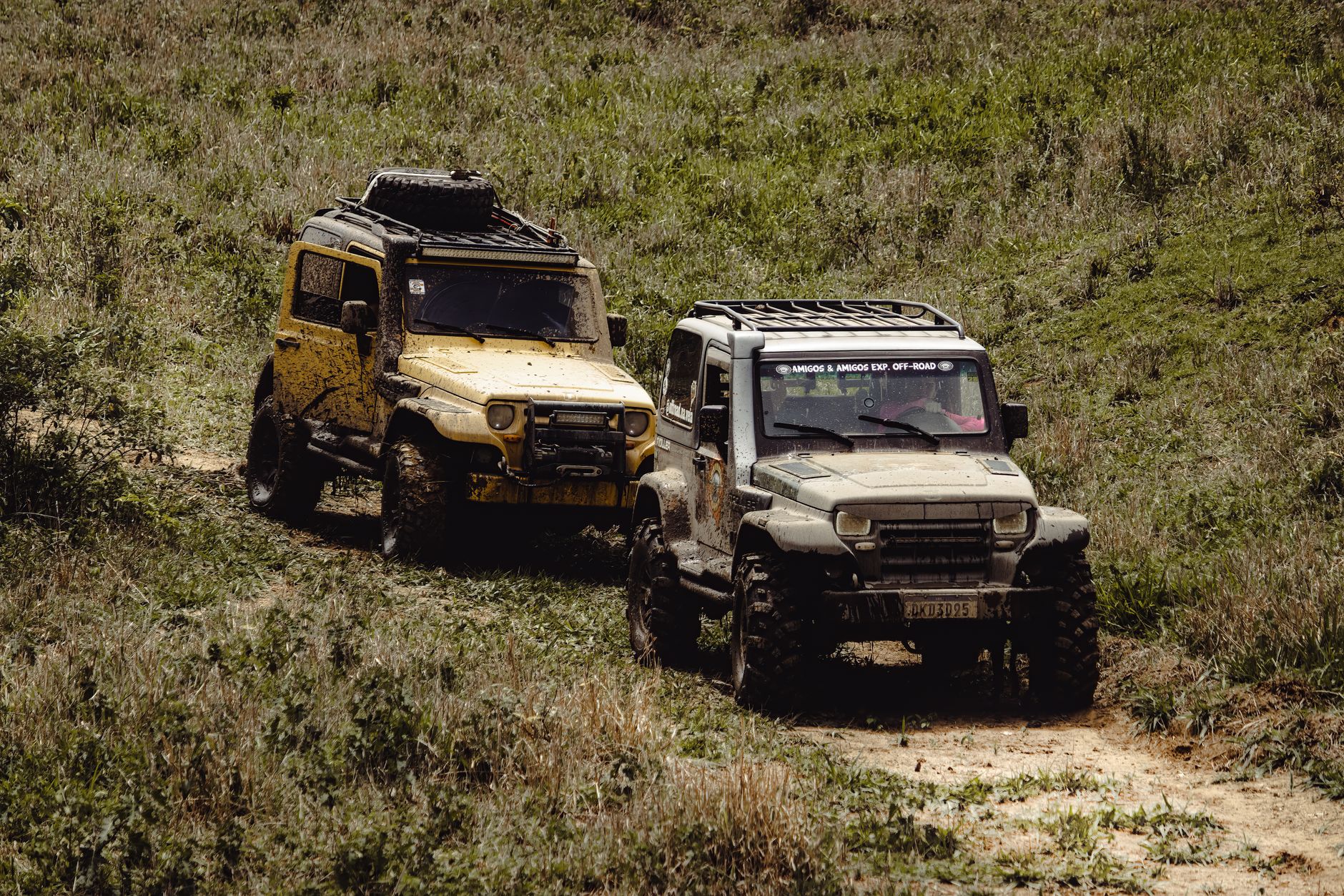 Two rugged 4x4 vehicles navigate a muddy path, showcasing off-road adventure spirit.
