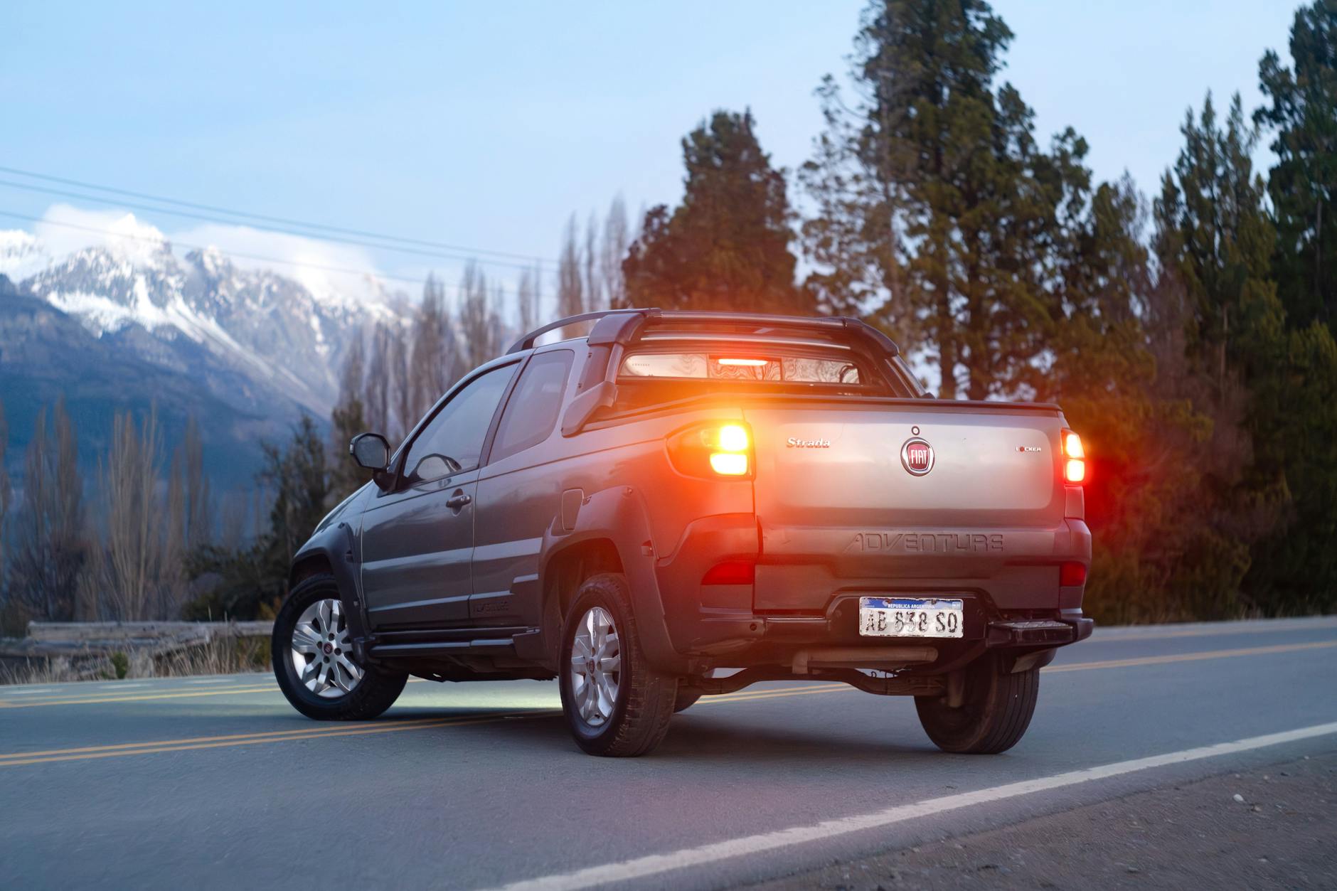 A silver pickup truck on a mountain road with snowy peaks in the background.