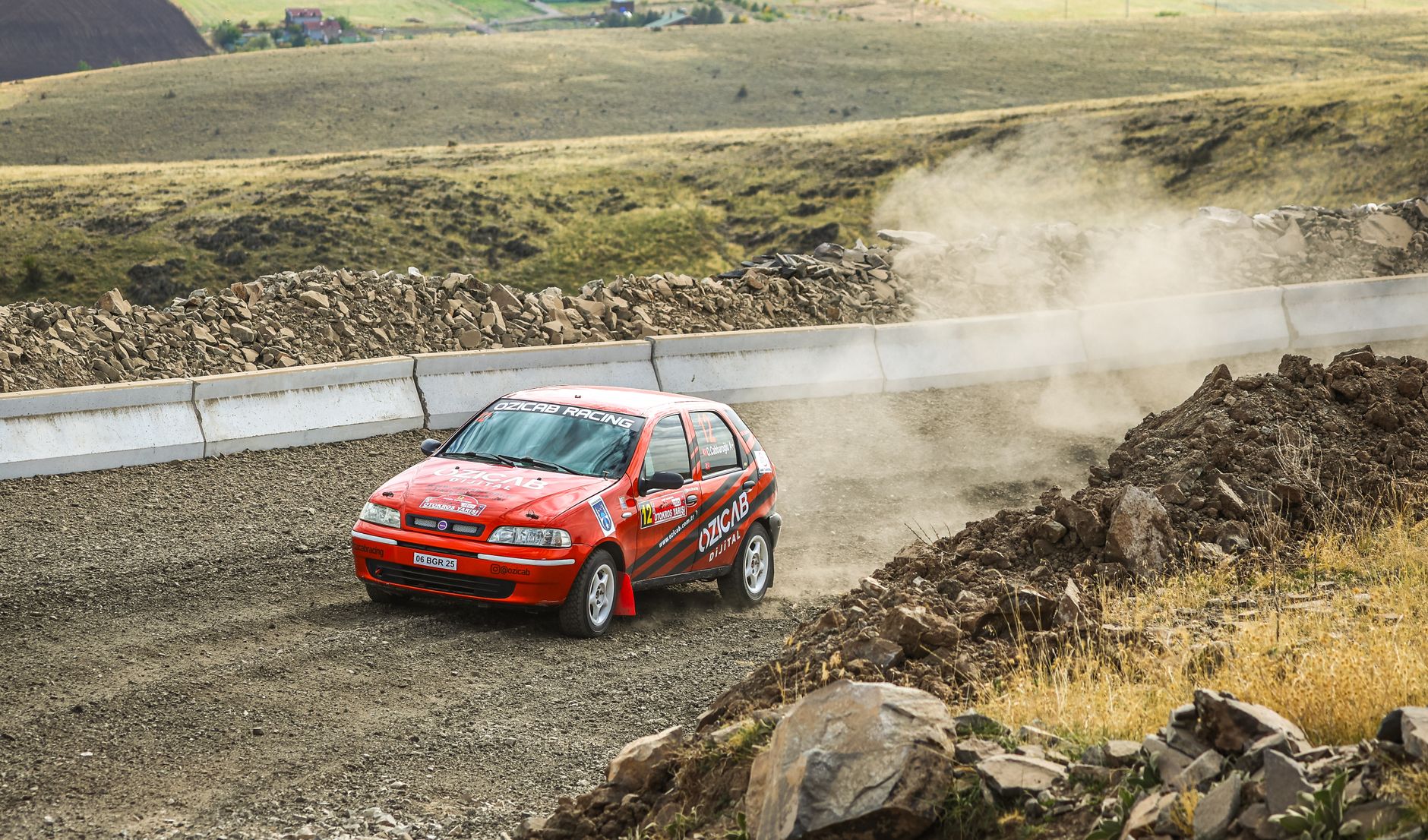Red Fiat rally car speeds around a curve on a dusty dirt track, creating dynamic motion.