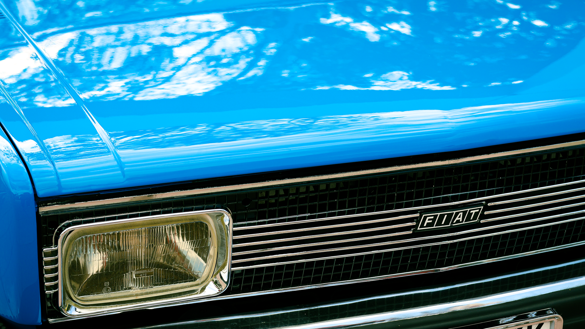 Detailed view of a vintage blue Fiat car grille with headlight and logo.