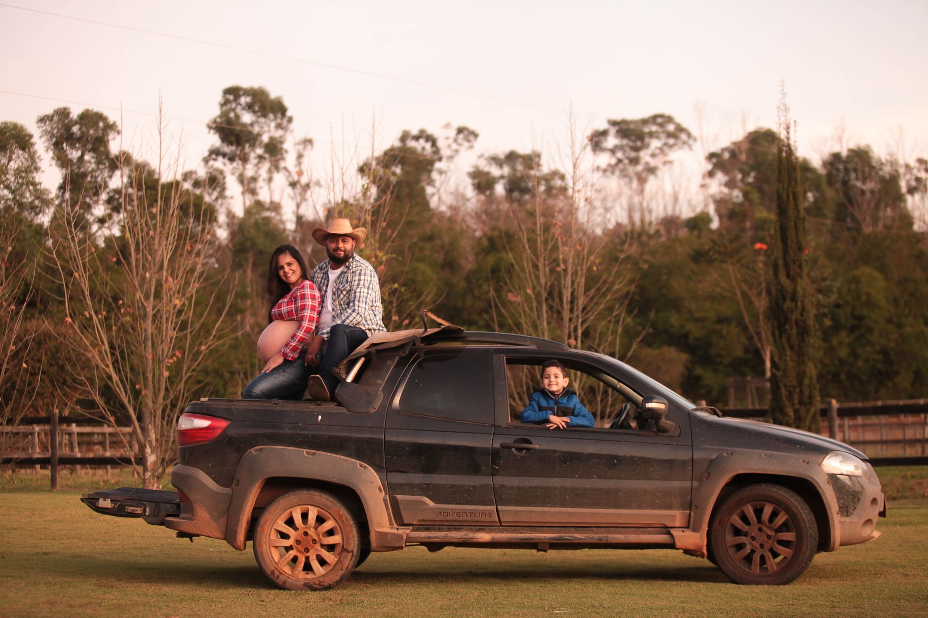 Smiling family enjoying a sunny day on a muddy pickup truck in the countryside.