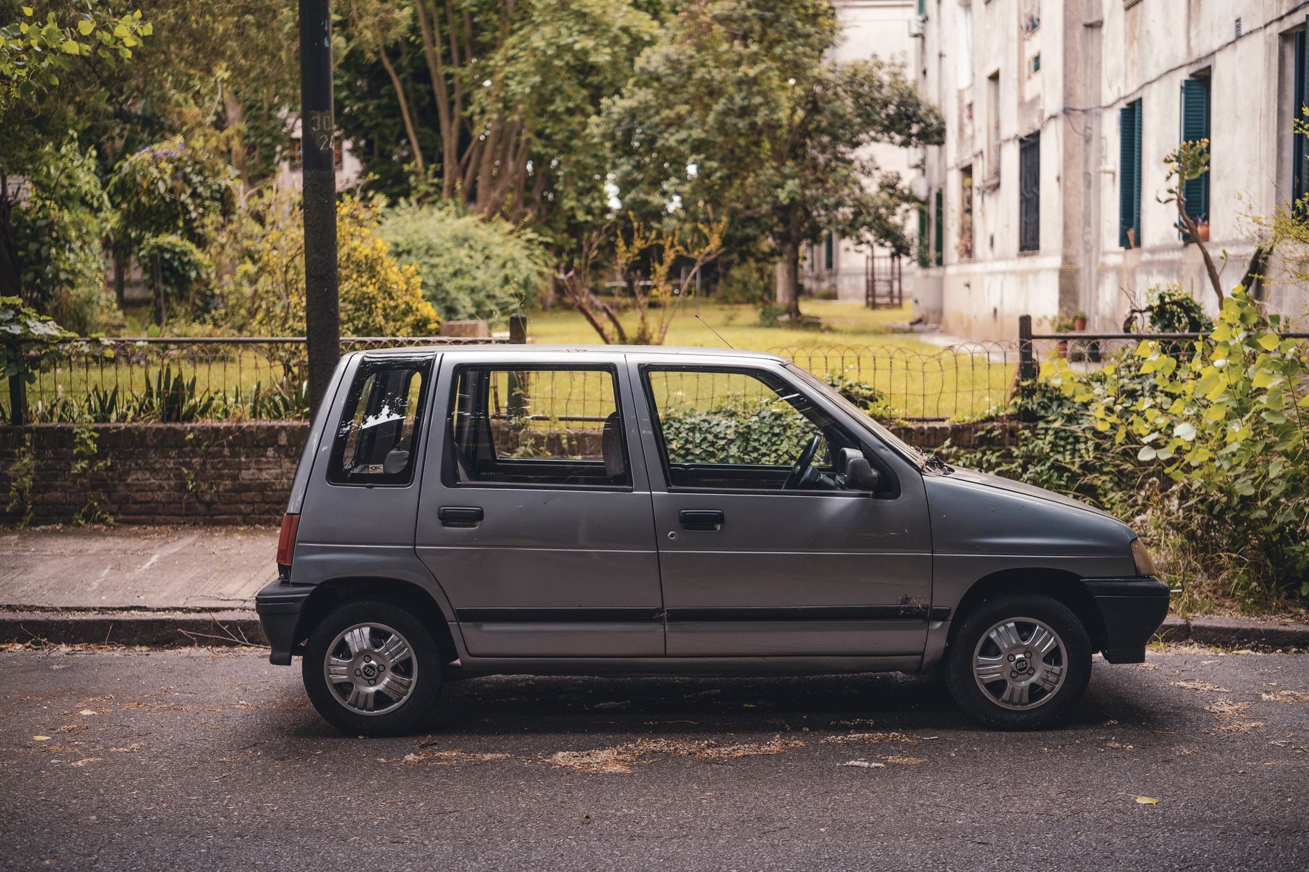 A classic compact car parked on a quiet city street surrounded by greenery.