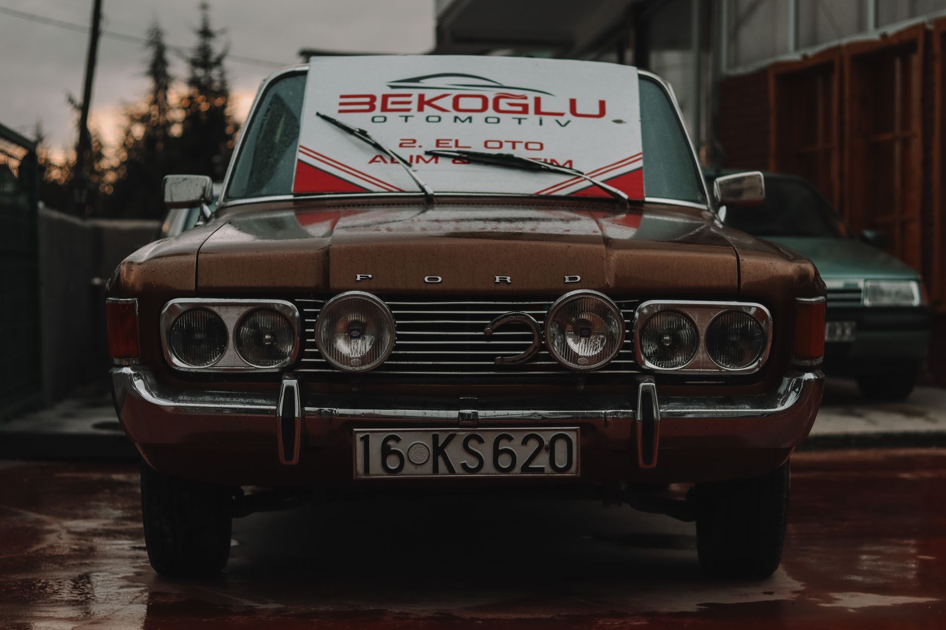 Classic Ford parked outdoors with a signage placard, captured on a rainy day.