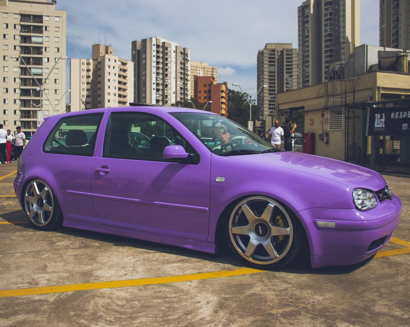 A tuned Volkswagen sports car in vibrant purple color parked in an urban cityscape.