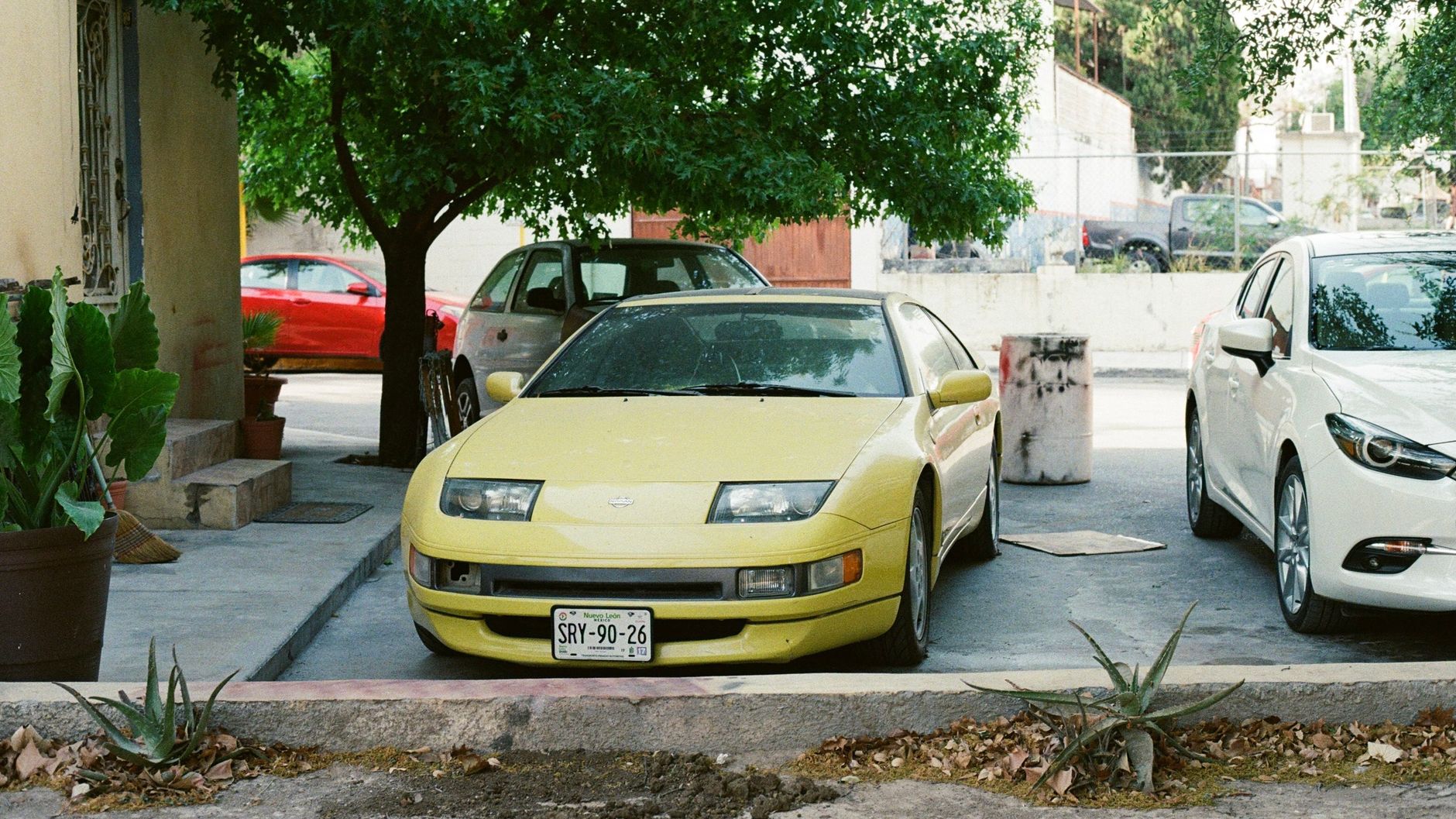 A vintage yellow car parked among other vehicles in a residential area.