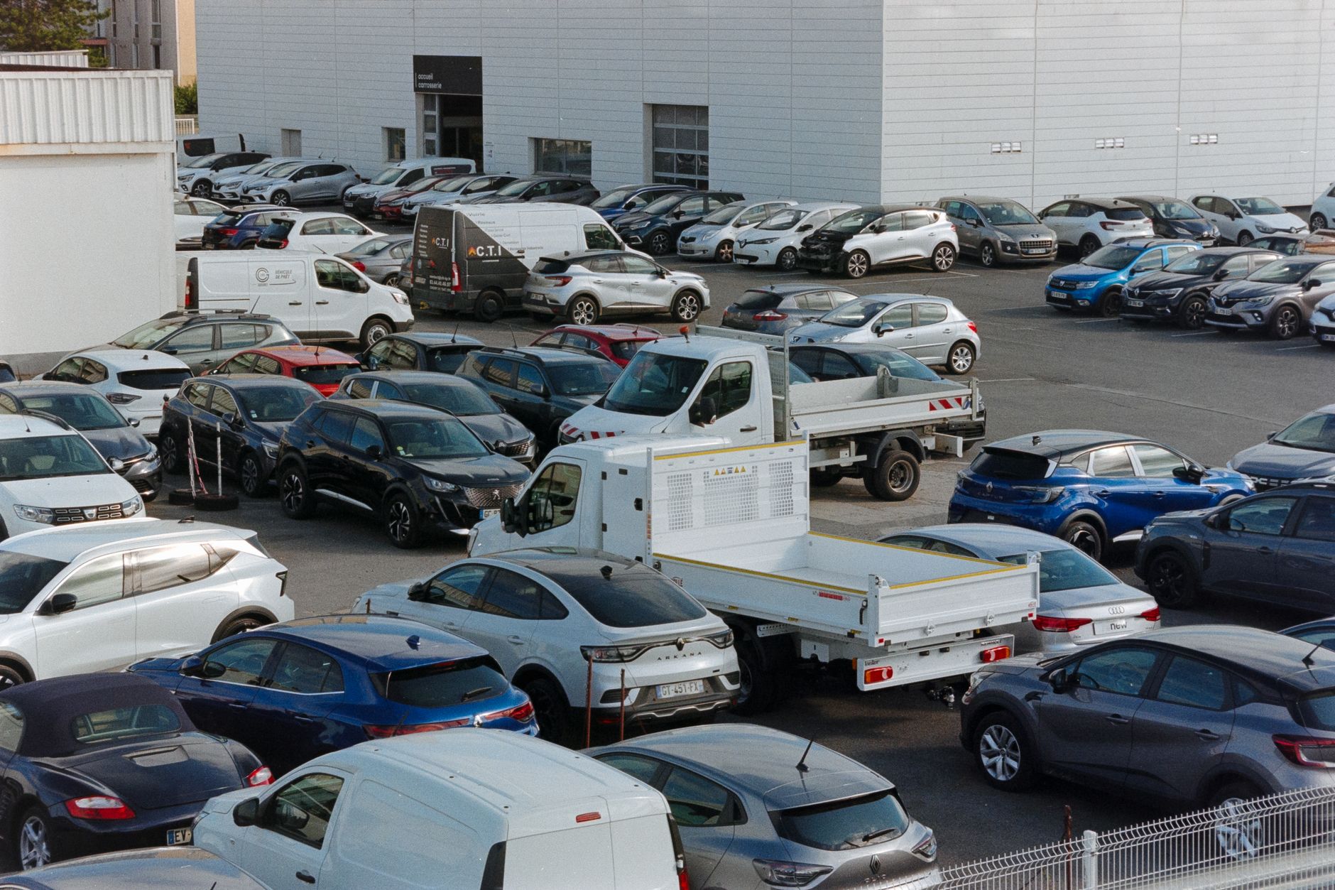 A crowded parking lot in Compiegne, France, featuring various parked cars and vans on a sunny day.