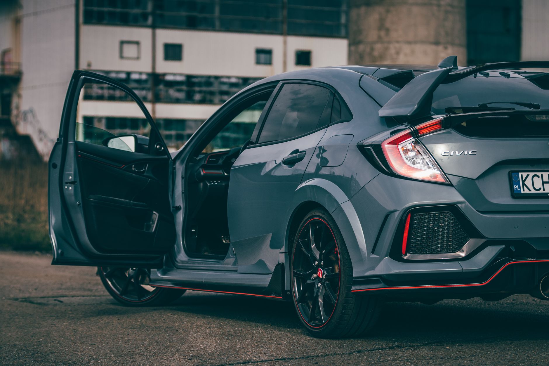 A stylish grey Honda Civic Type R with door ajar, showcasing its sporty features in an urban environment.