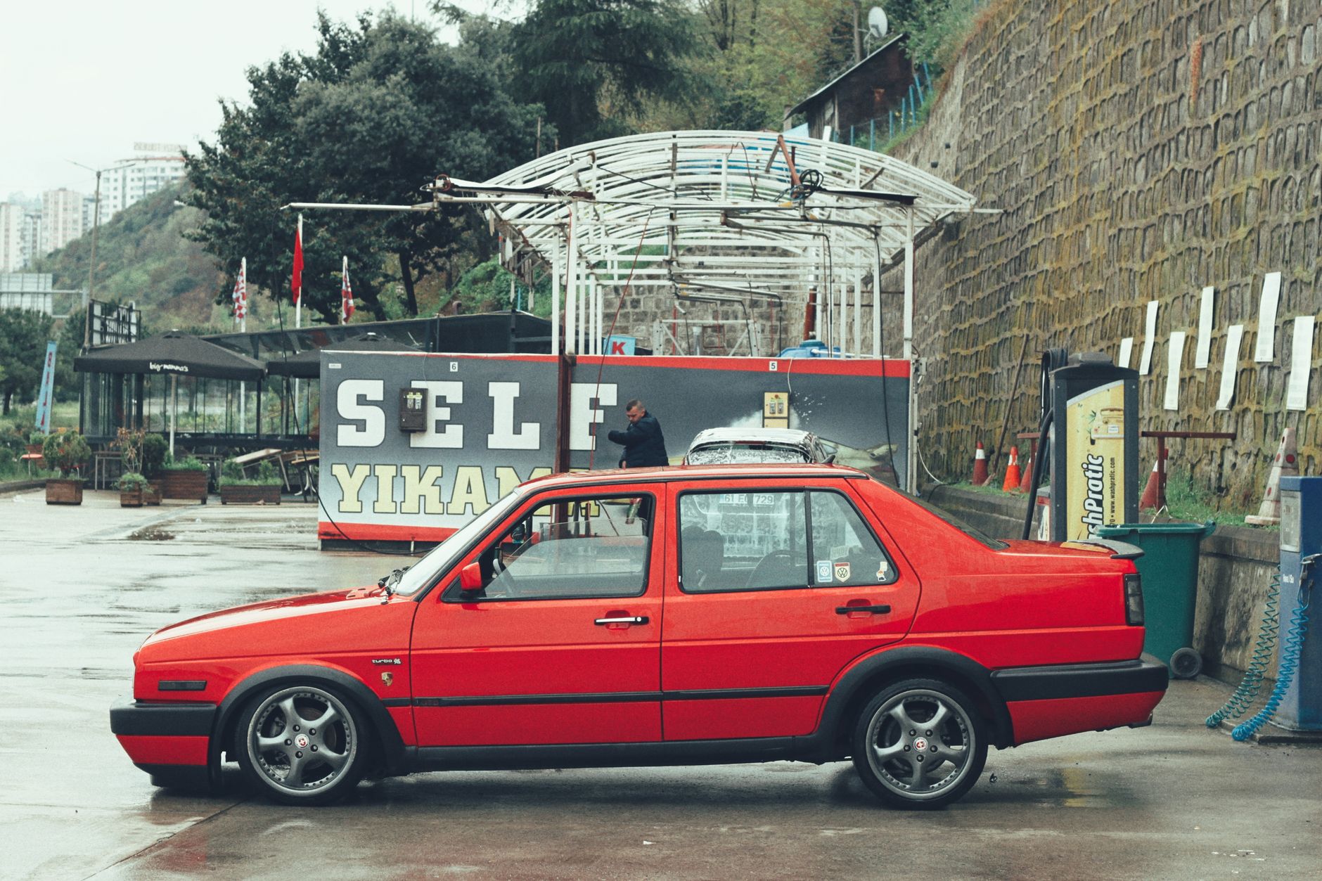 A vintage red Volkswagen car parked at an outdoor self-service car wash in Turkey.