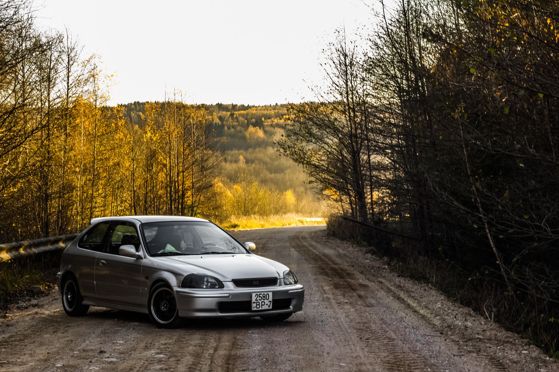 A silver car parked on a scenic dirt road surrounded by autumn trees in Belarus.