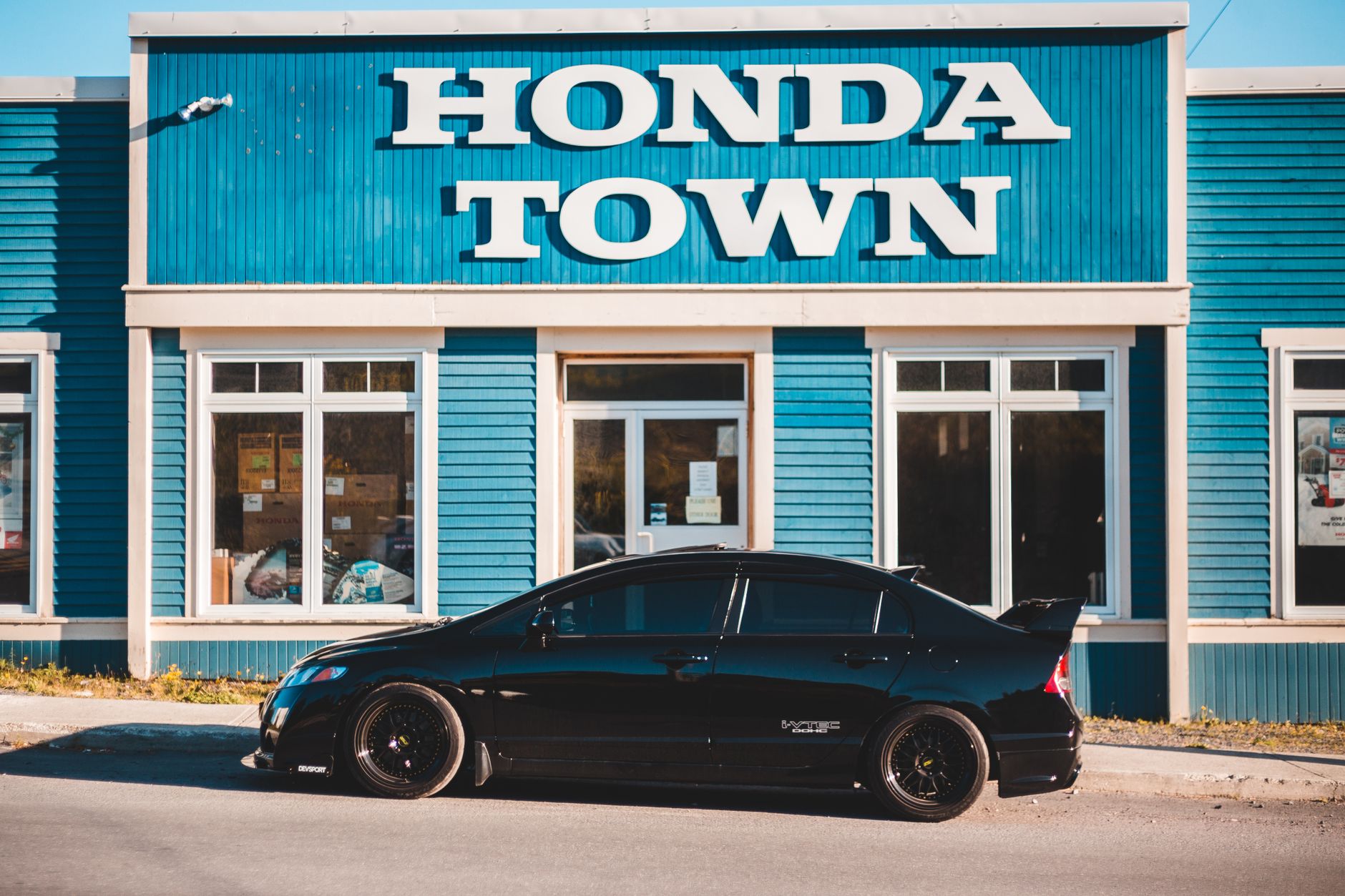 Side view of modern black automobile parked near store with blue exterior with shop sign in daylight in street outside
