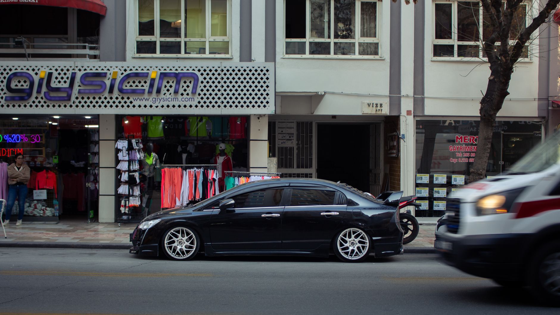 A sleek black sedan parked on city street in front of colorful clothing store.