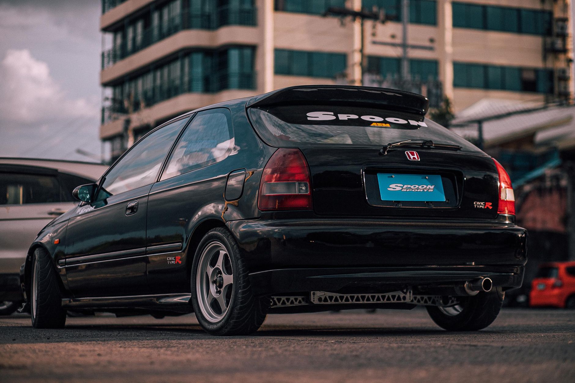 Rear view of a black Honda Civic parked on a city street under cloudy sky.