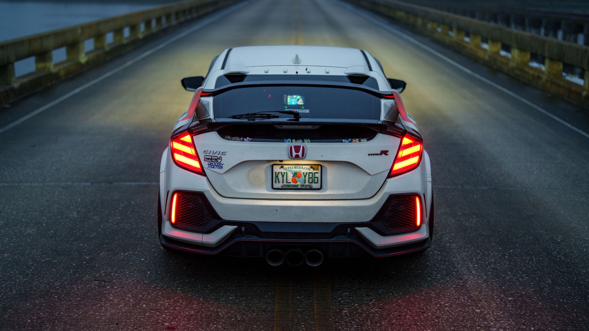 Sporty white car with taillights on a bridge road during twilight or night.