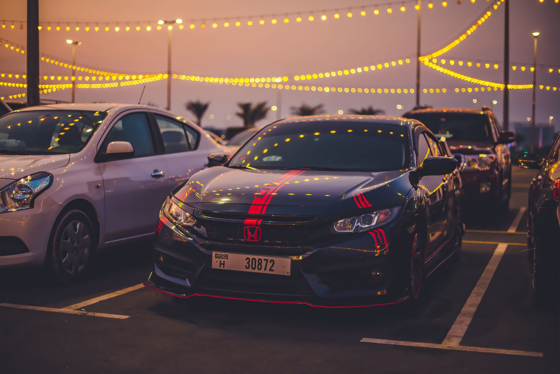 Honda Civic car parked under decorative lights in a vibrant parking lot during twilight.