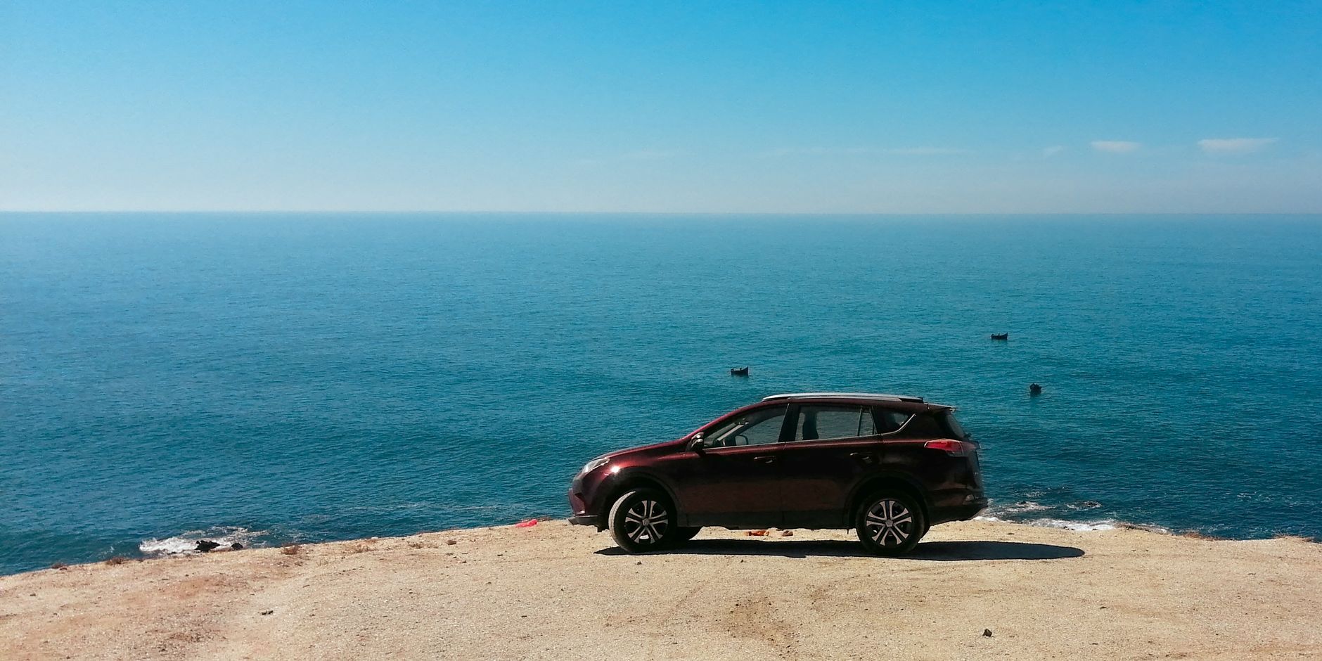 Red SUV parked on a cliff edge with a serene ocean view in Sidi Ifni, Morocco.