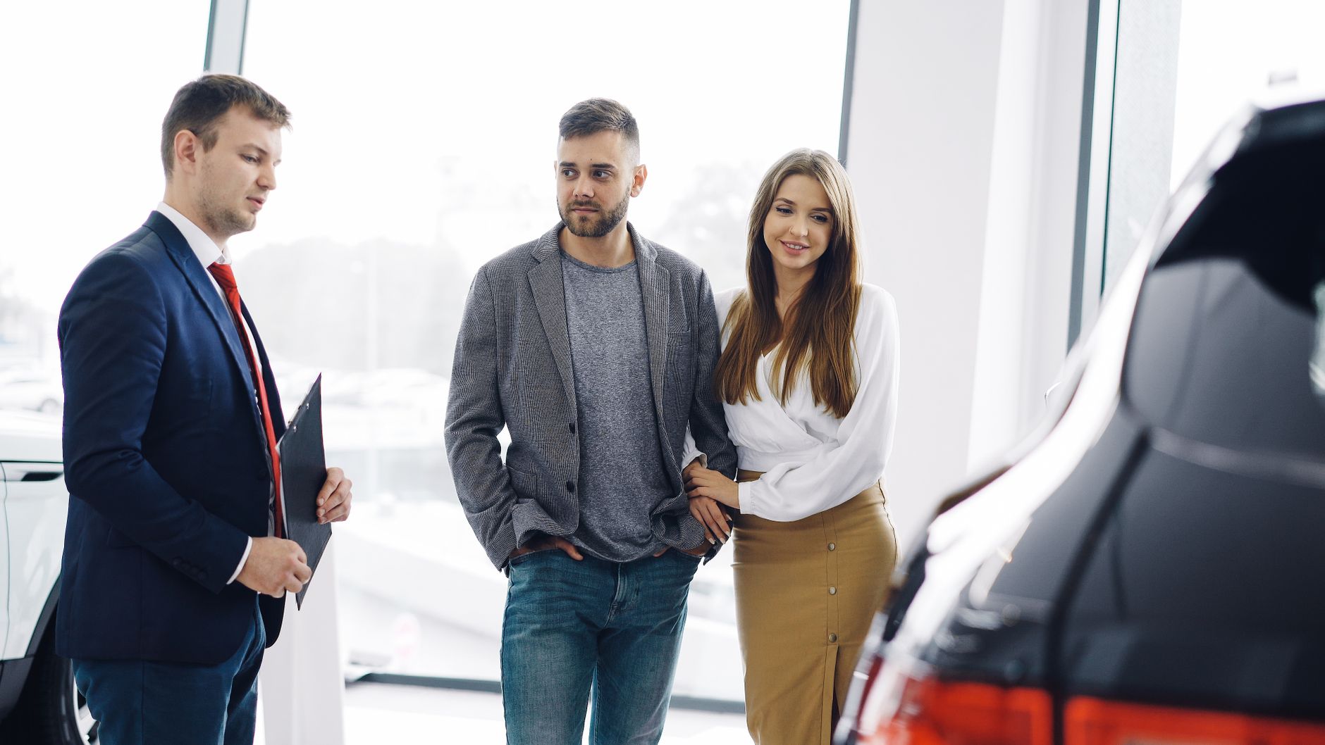Smiling couple with salesman in car showroom discussing features of a car.