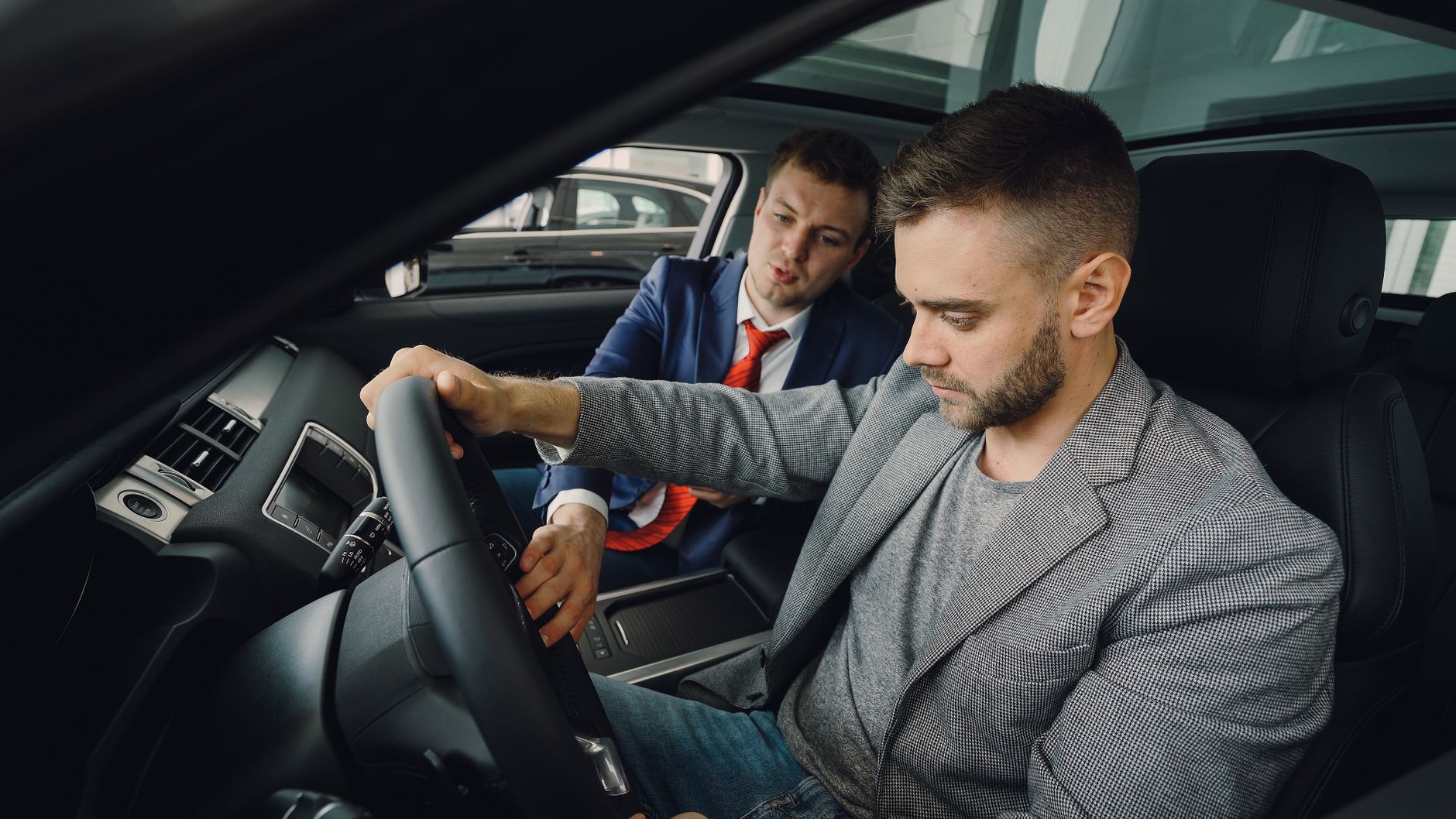 Salesman demonstrating car features to potential buyer inside vehicle showroom.