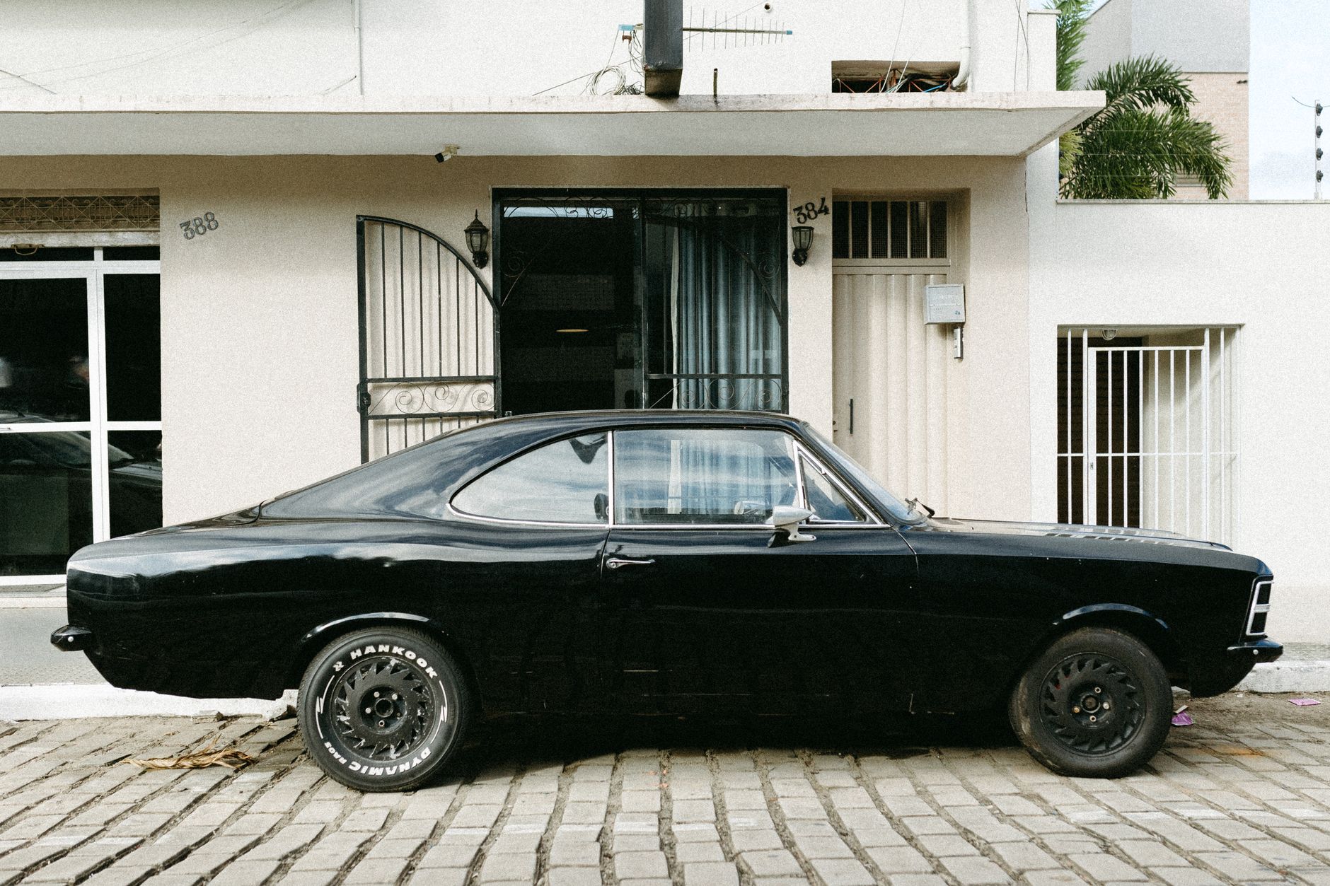 Retro black Chevrolet Opala parked on cobblestone pavement in front of urban houses.