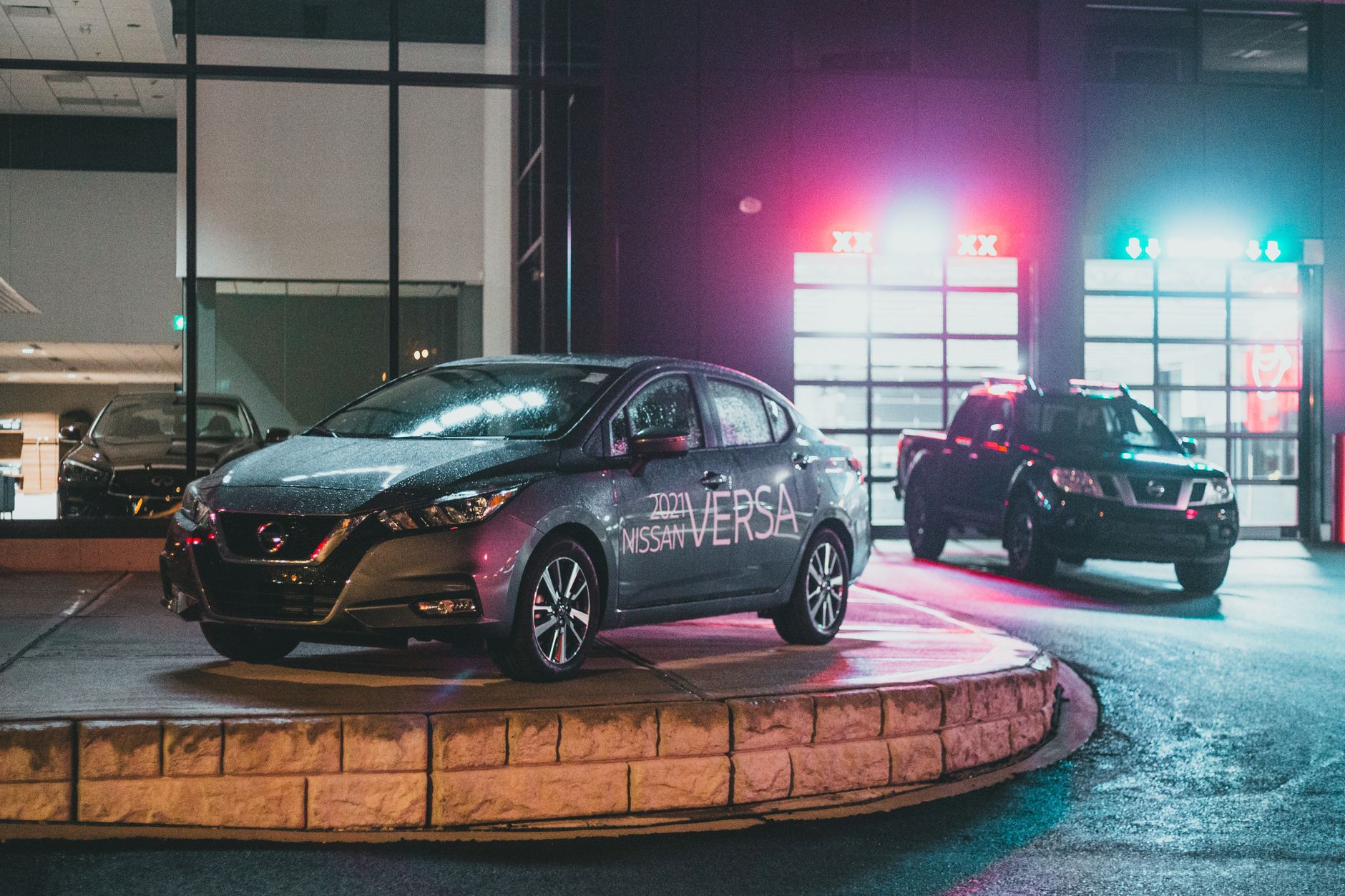 Contemporary dark vehicles placed on pavement in car dealership near glowing glass wall at night