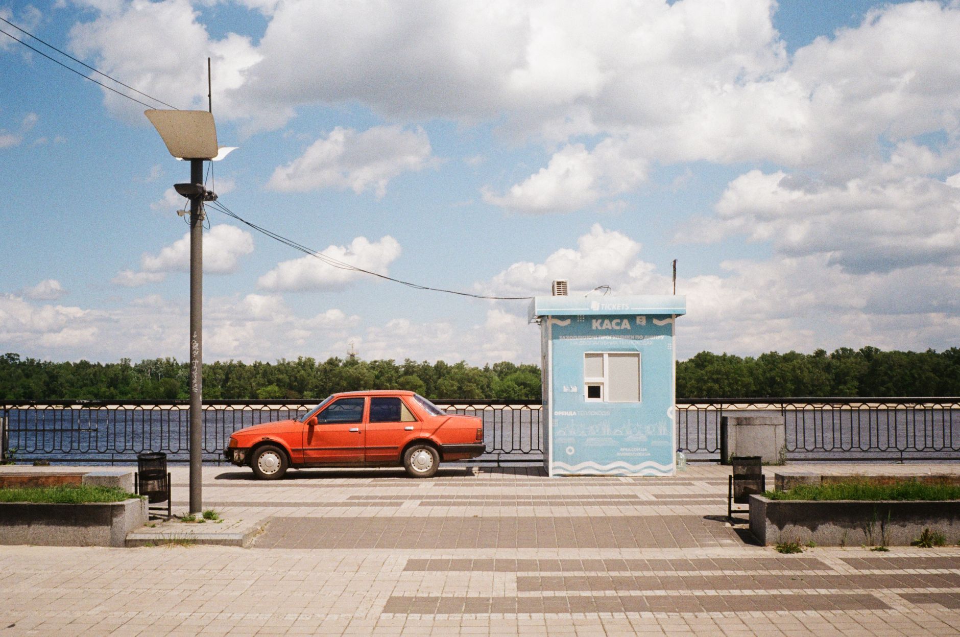 Retro red car parked next to a blue booth by the Dnipro River in Kyiv.