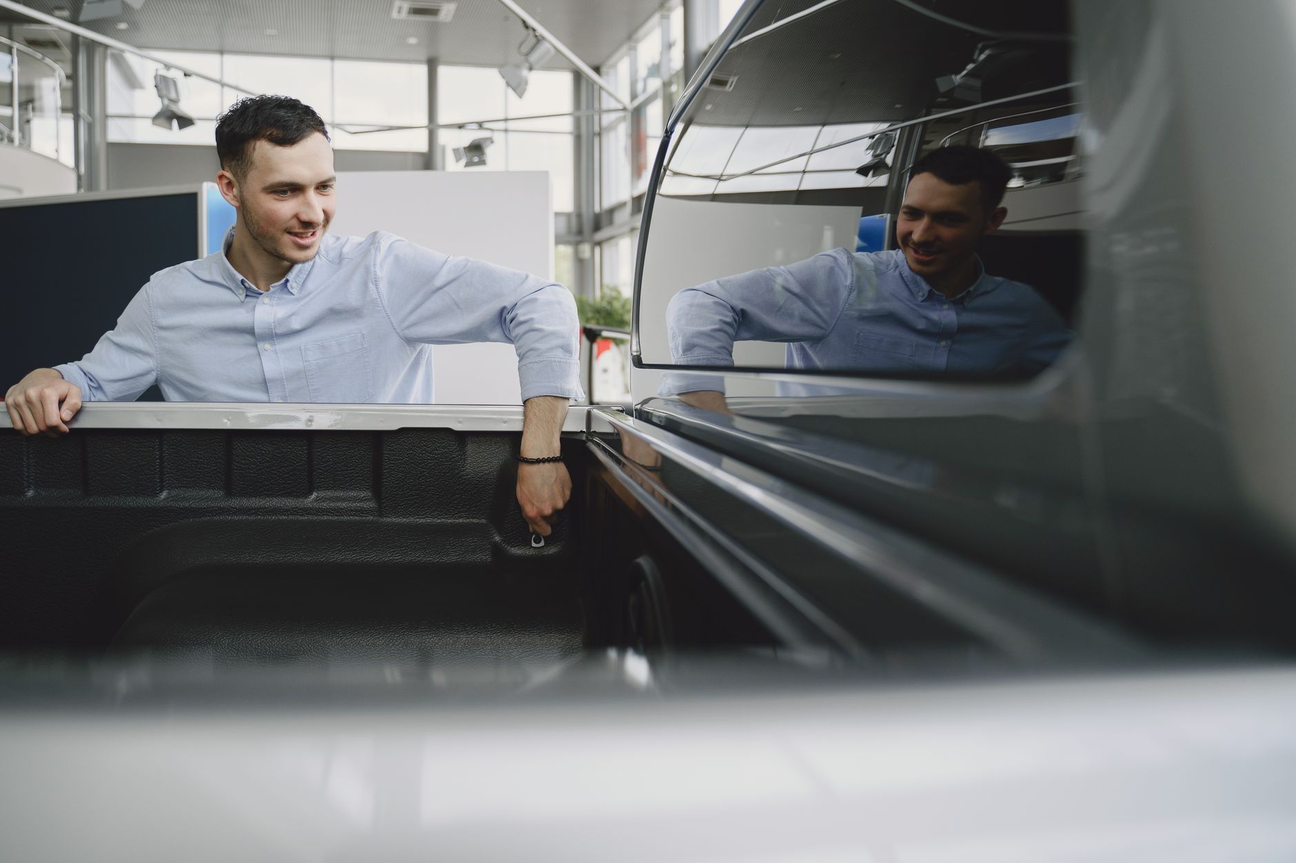 Man in a showroom examining the bed of a pickup truck, reflecting natural curiosity.