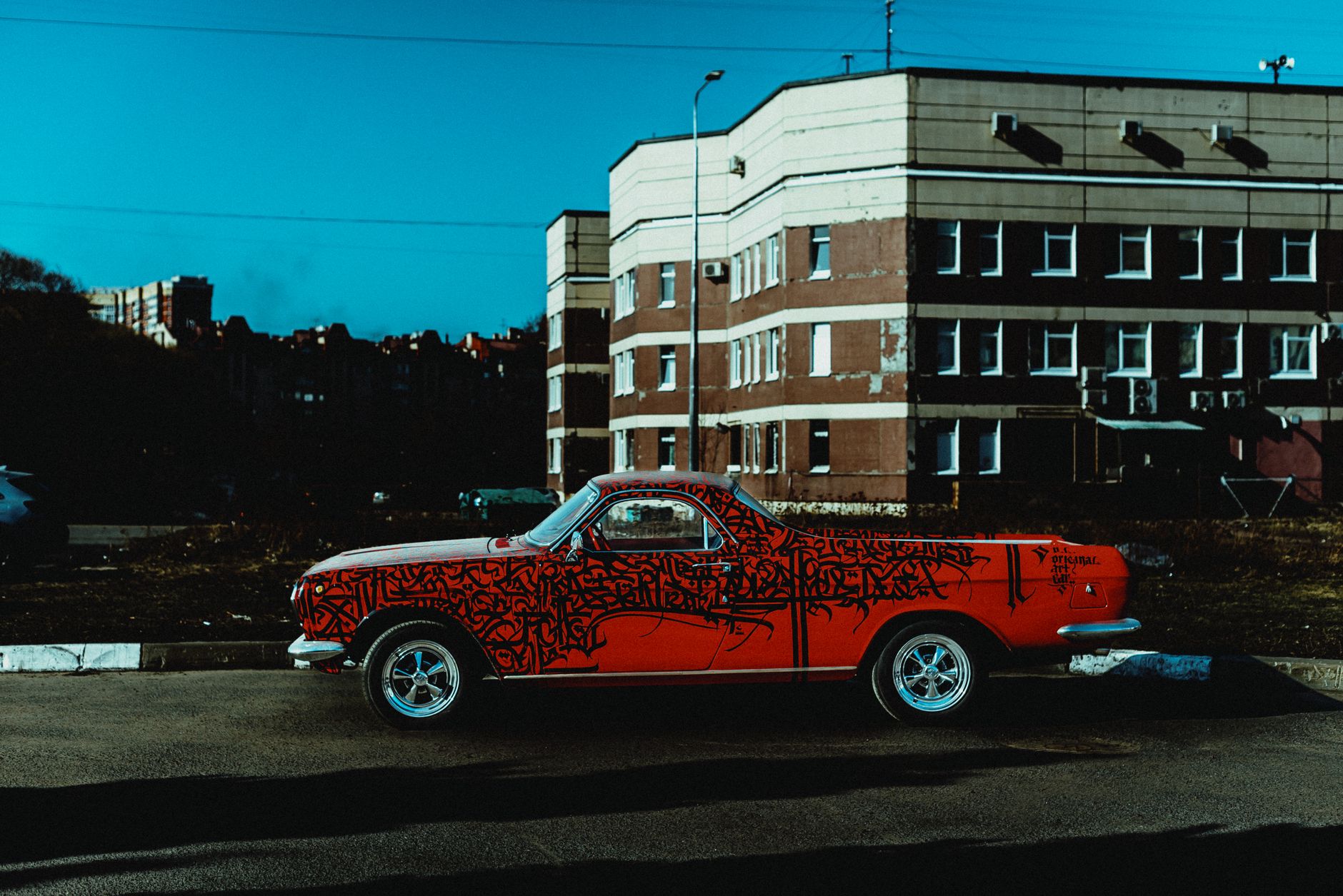 A custom vintage red pickup truck with graffiti standing on a city street, against building exteriors.