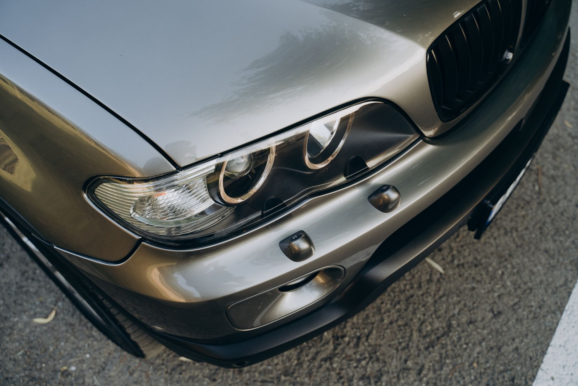 A detailed close-up of a silver sports car headlight showcasing its sleek design on an outdoor setting.