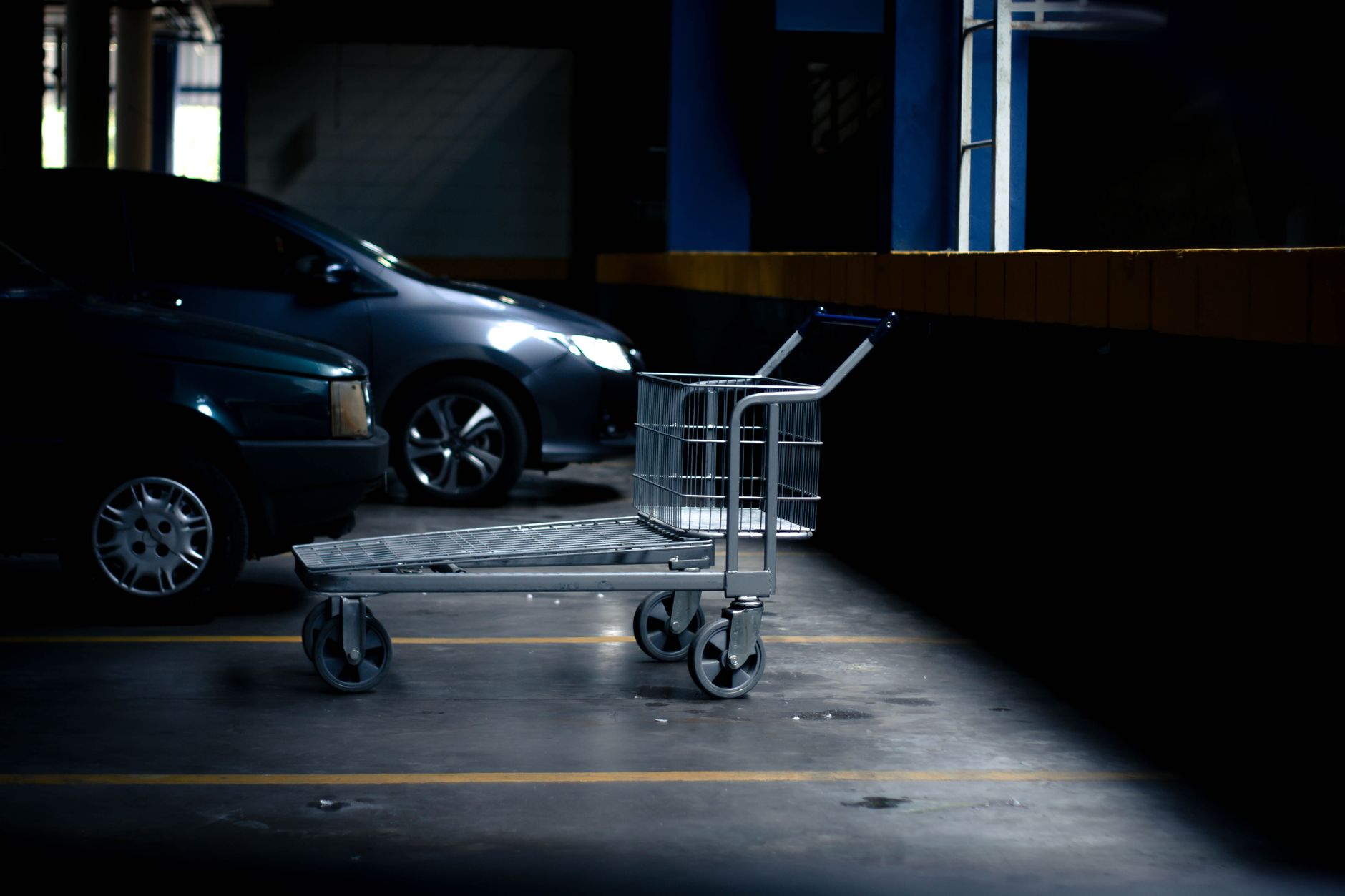 Lonely shopping cart in a dimly lit parking garage next to parked cars.