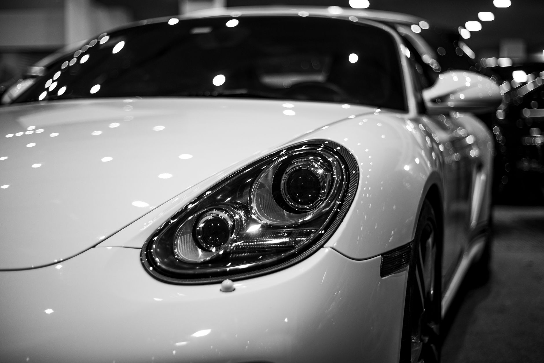 Black and white image of a luxury car under showroom lights, showcasing elegance and style.