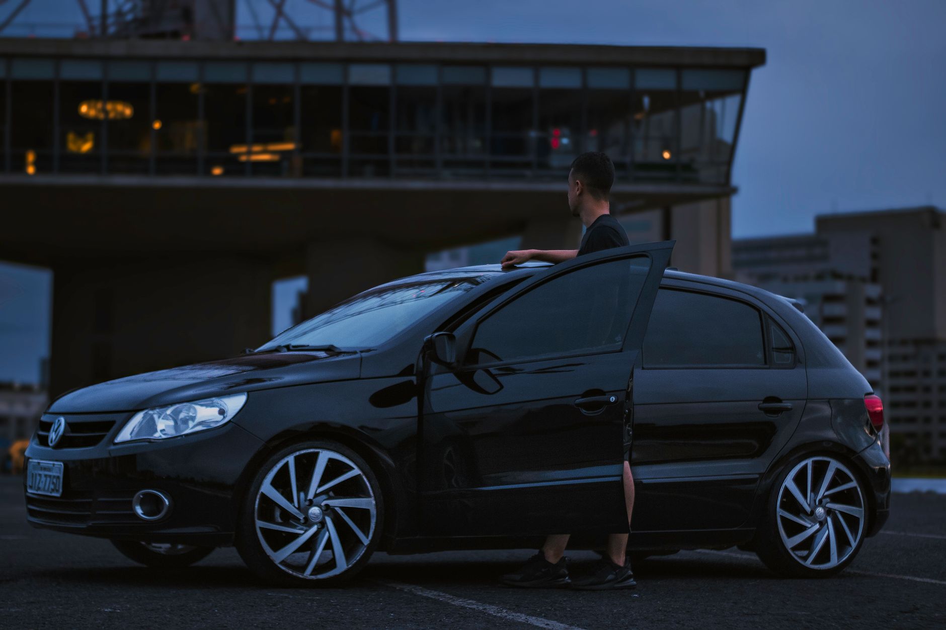 A sleek black hatchback with a person standing beside it in an urban evening setting in Brasília.