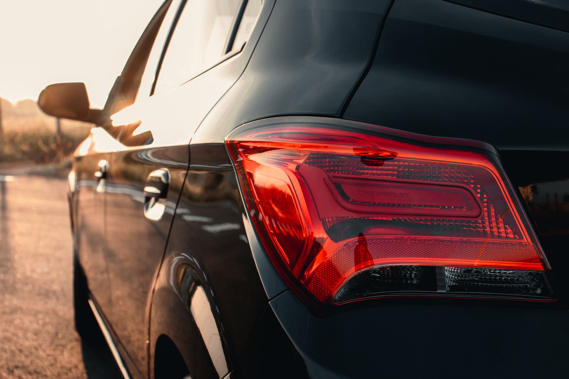 Detailed view of a black car's taillight illuminating at sunset, showcasing modern design.