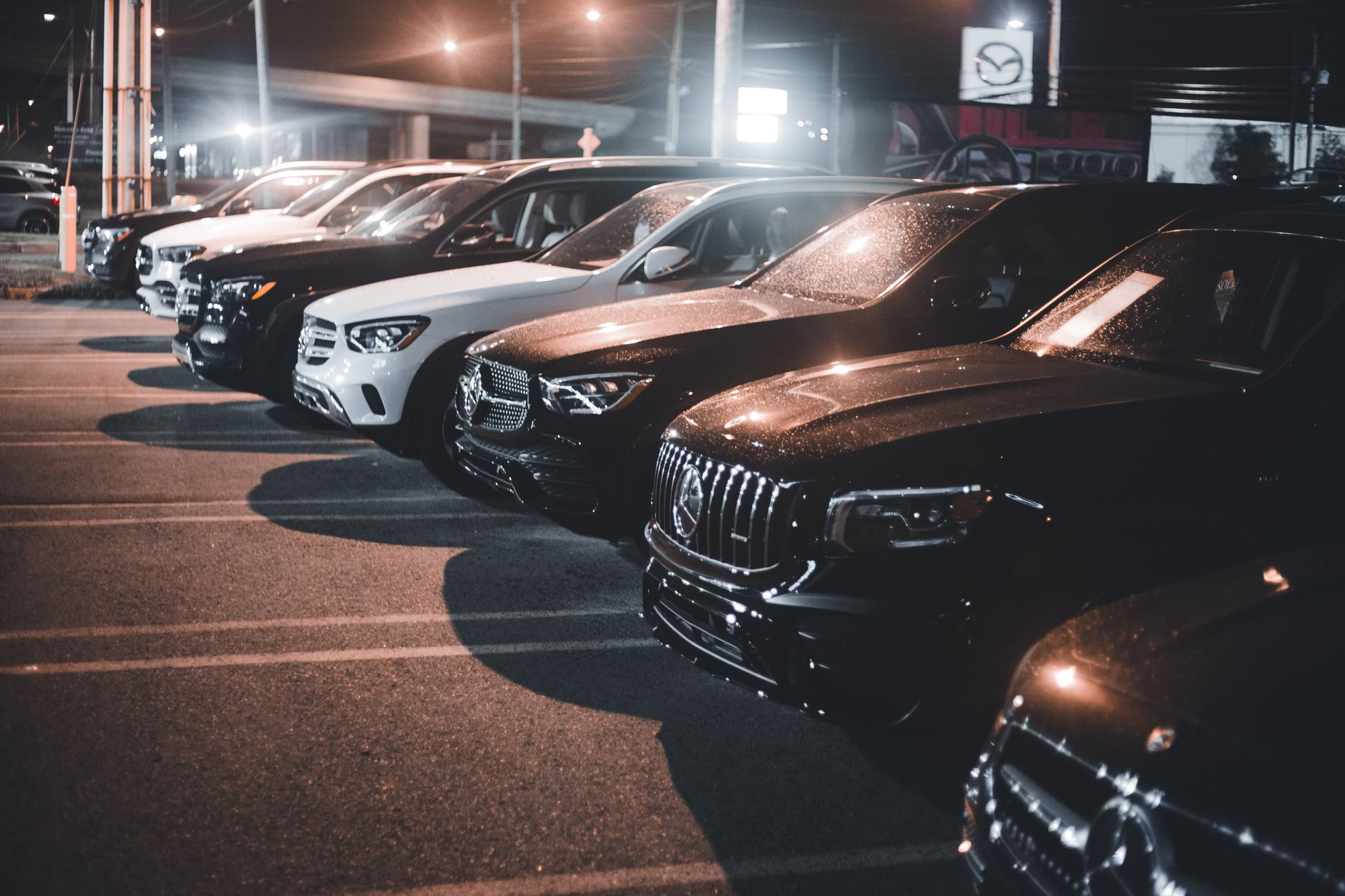 Row of luxury cars in a parking lot at night, illuminated by streetlights.