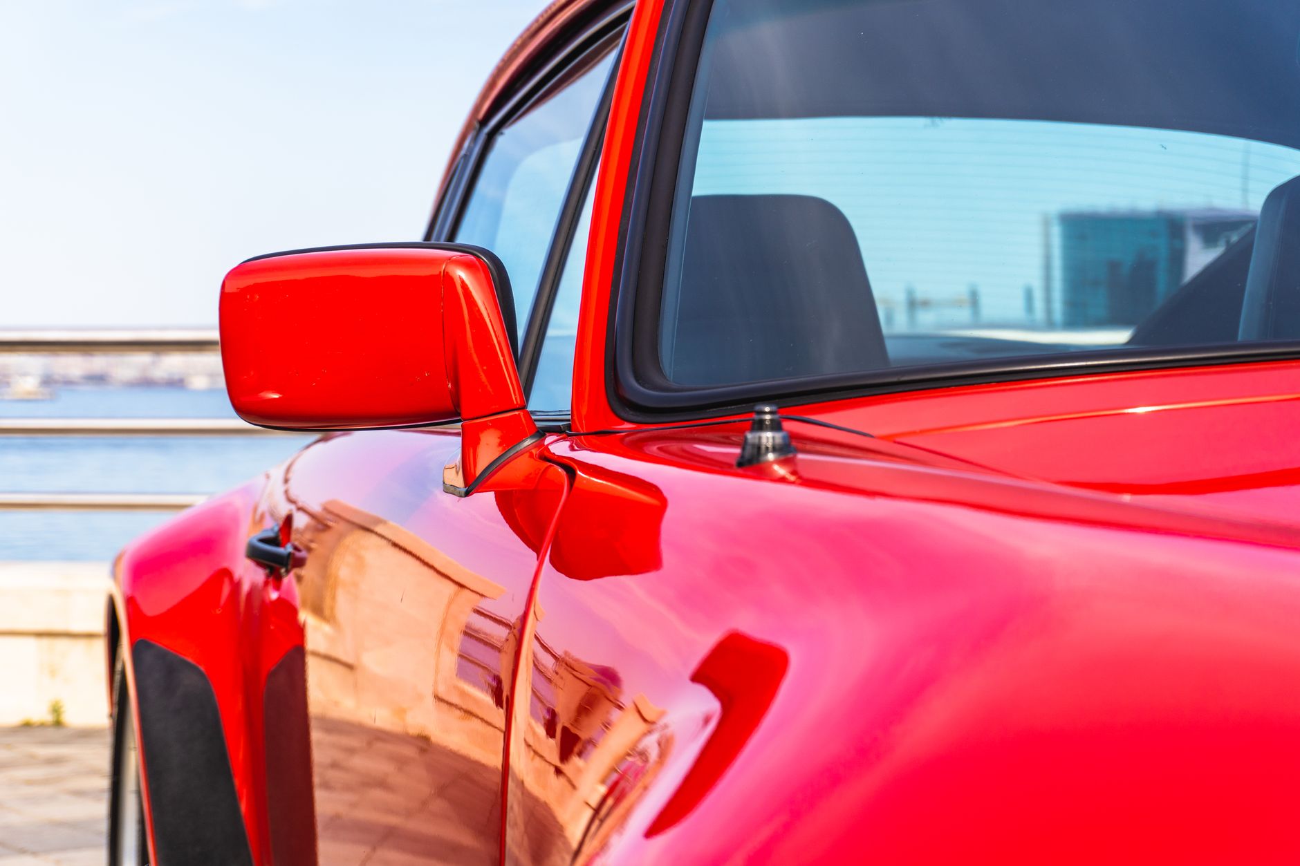 Detailed view of a shiny red sports car's side mirror and fender, photographed outdoors in Baku.