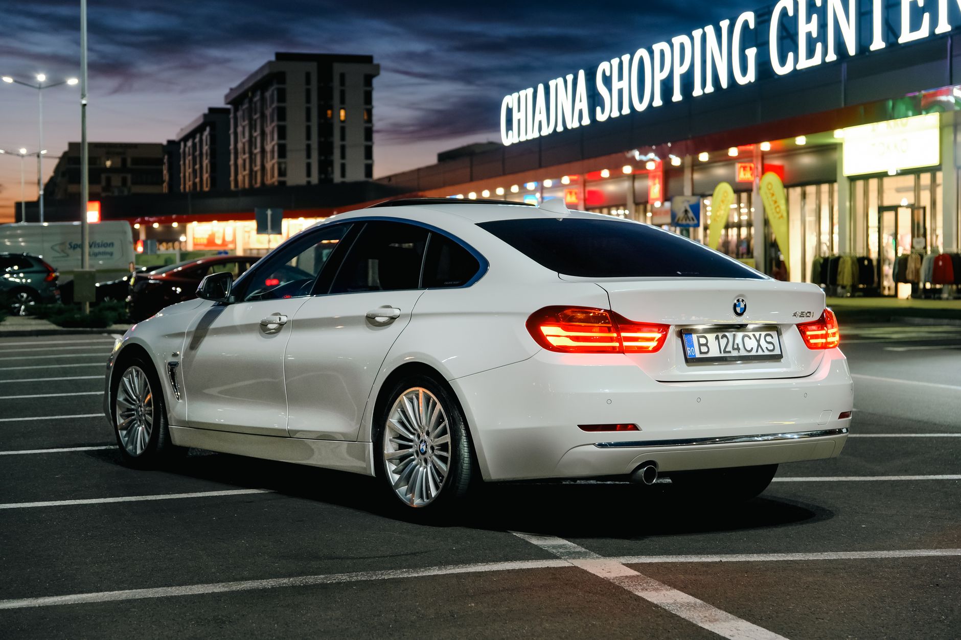 A luxury white car parked in front of Chiajna Shopping Center at twilight.