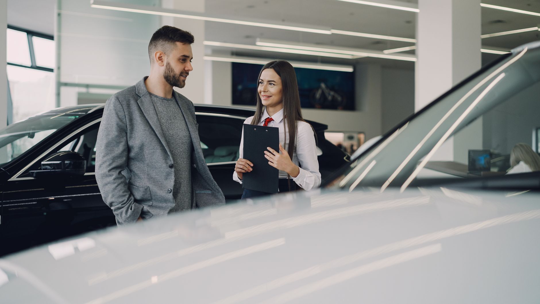 Man consults with salesperson in modern car dealership showroom.