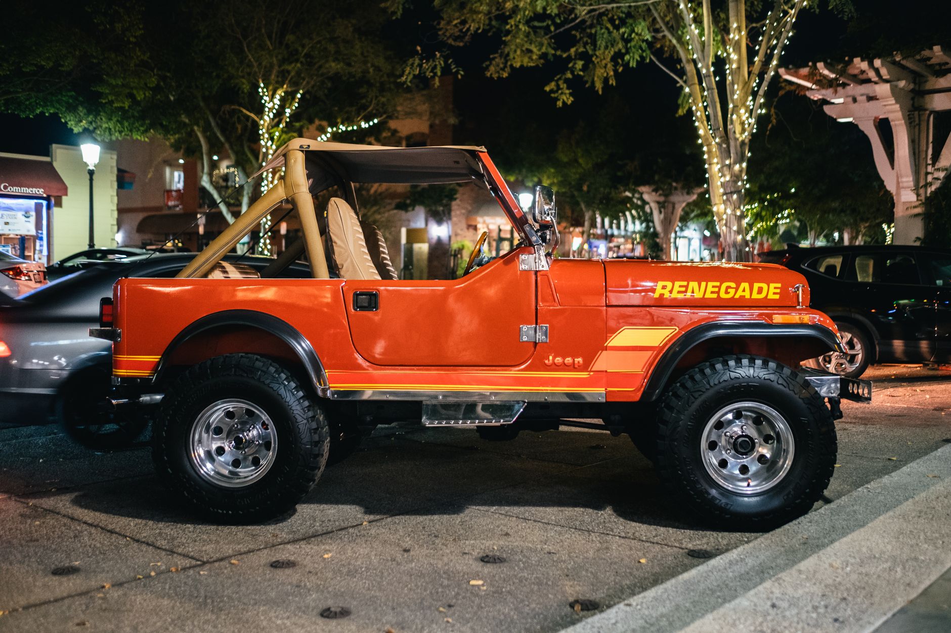 Vibrant red Jeep Renegade parked on a well-lit street under trees with festive lights.