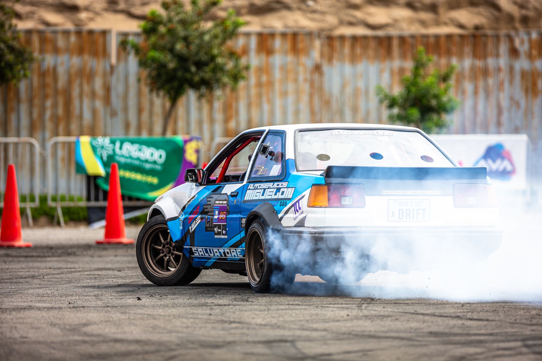 A classic Toyota AE86 performs a drift maneuver on a track, emitting smoke.