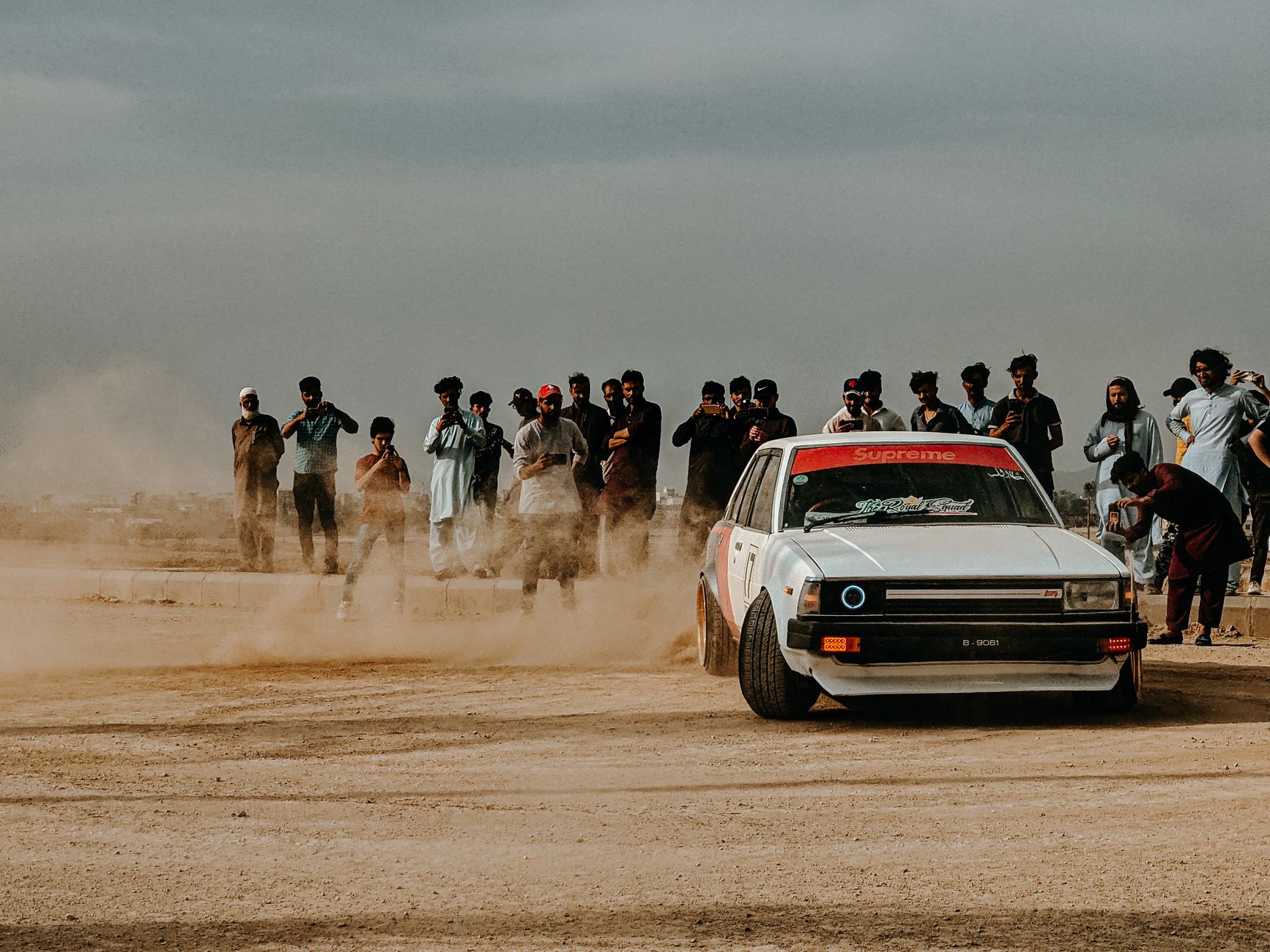 Energetic car drifting scene with a Toyota Corolla E70 in the desert captured with spectators.